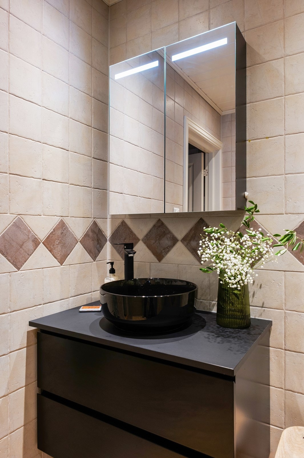 Videre er badet utstyrt med servantskap med skuffeinnredning, benkeplate med ovenpåliggende servant og speilskap med integrert belysning over Galleribilde