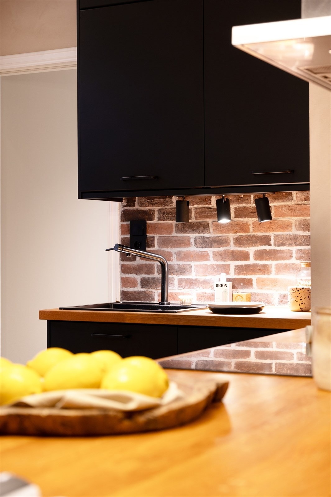 Innredning med mørke, glatte skapfronter, benkeplater i tre, nedfelt oppvaskkum og ett-greps armatur, begge i sort utførelse Galleribilde