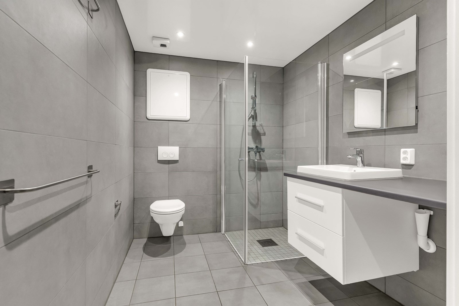 Baderommet er utstyrt med dusjhjørne med glassdører, opplegg for vaskemaskin og vegghengt toalett, samt servantskap med nedfelt servant, underskuffer og 1-greps blandebatteri. Galleribilde