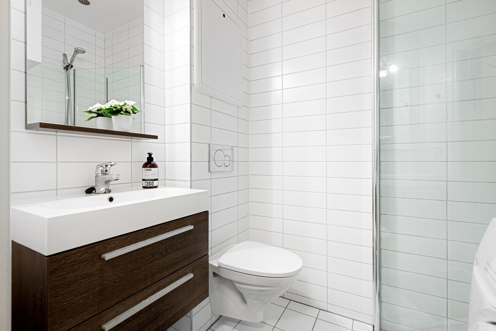 Badet er utstyrt med vegghengt toalett, servant med servantskap, speil med belysning, samt veggmonterte dusjvegger i herdet glass. Galleribilde