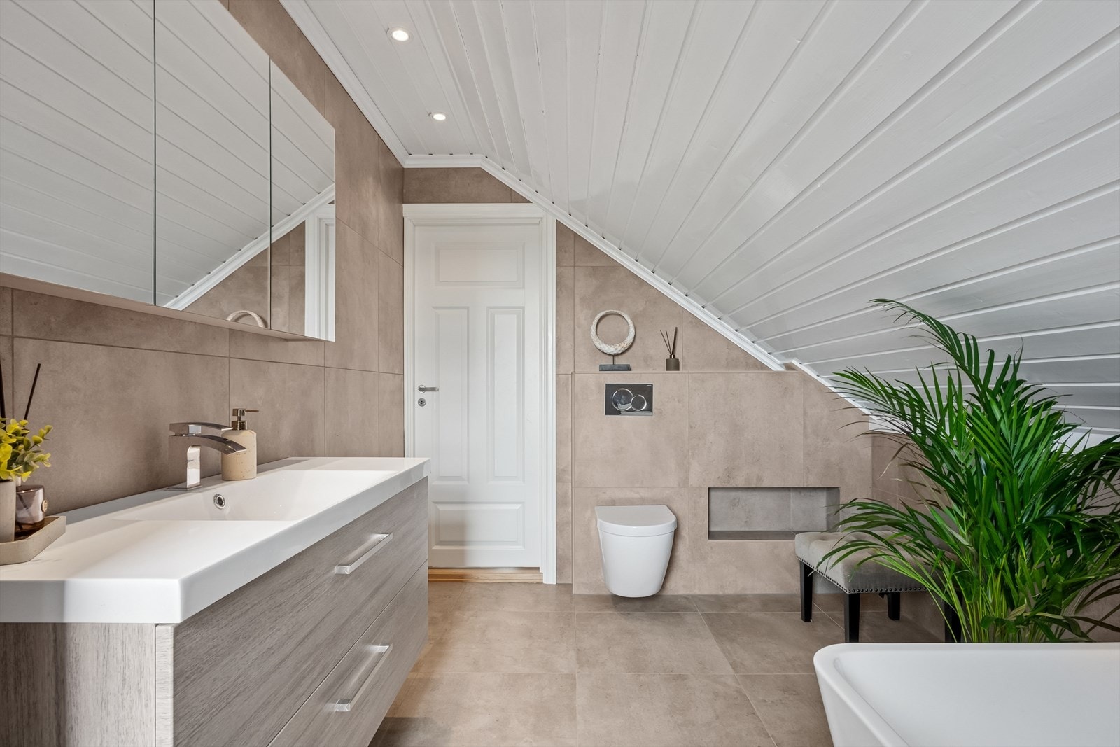 Det er elektriske varmekabler i gulvet. Rommet er videre utstyrt med baderomsinnredning med servant, veggmontert toalett og badekar. Det er også balansert ventilasjon her. Galleribilde