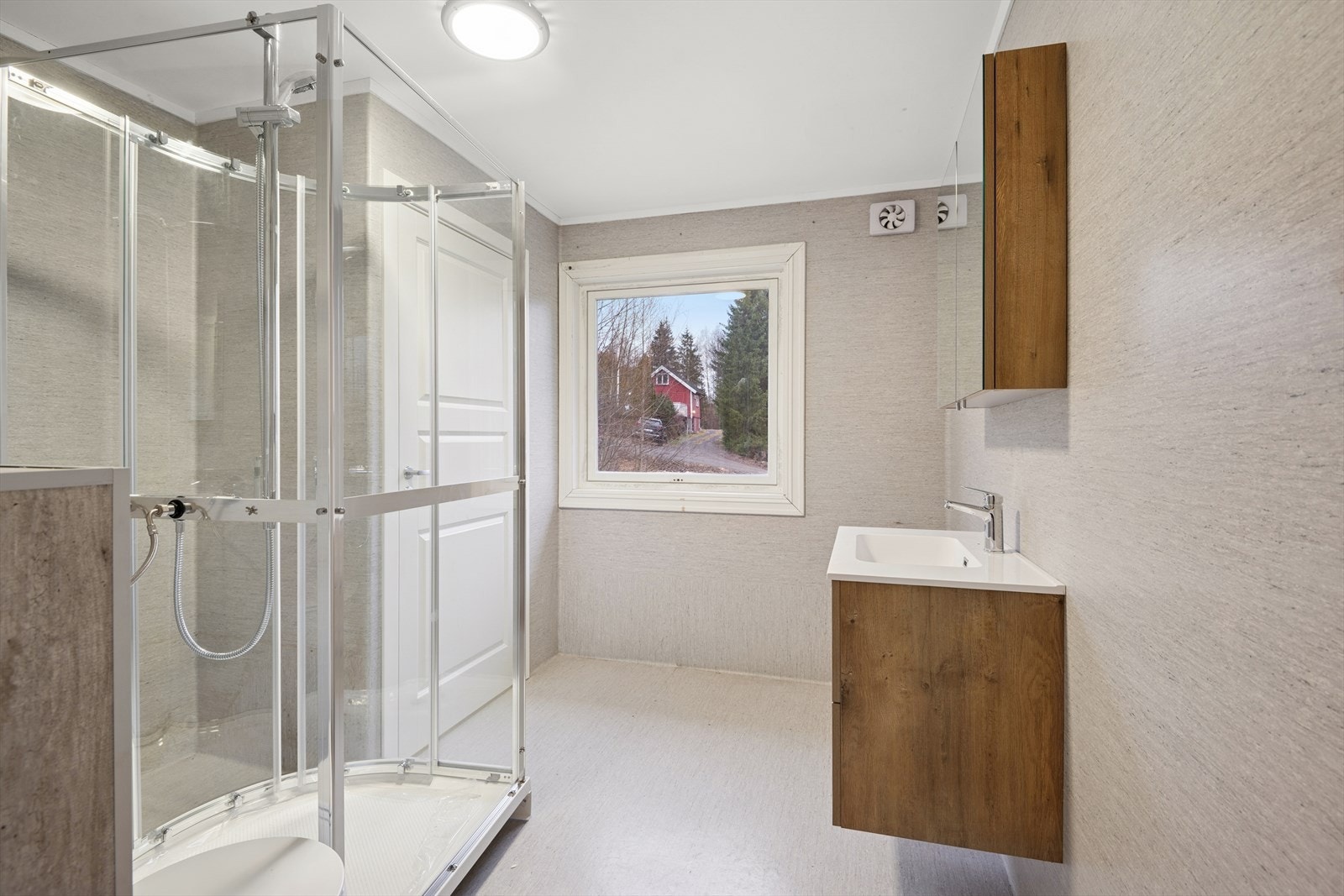 Badet har våtromstapet/belegg på vegger, malt tak og vinylbelegg med elektriske varmekabler på gulv. Rommet er innredet med servant, veggmontert toalett, dusjkabinett og opplegg for vaskemaskin. Galleribilde