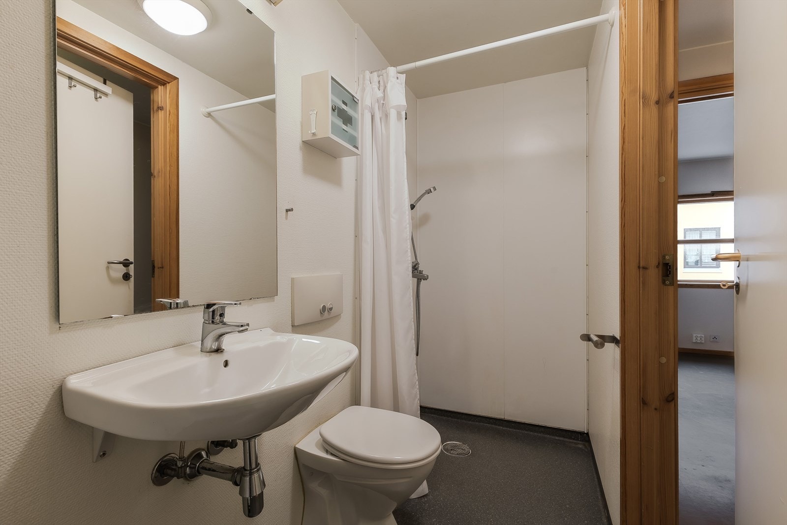 Enkel innredning på bad med dusj, vask, toalett og opplegg for vaskemaskin Galleribilde