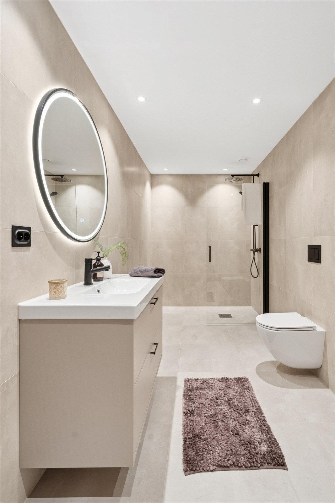 Det vegghengte toalettet bidrar til et stilrent og ryddig utseende, mens dusjgarnityret med både takdusj og justerbar hånddusj gir fleksibilitet og komfort under dusjingen. Galleribilde