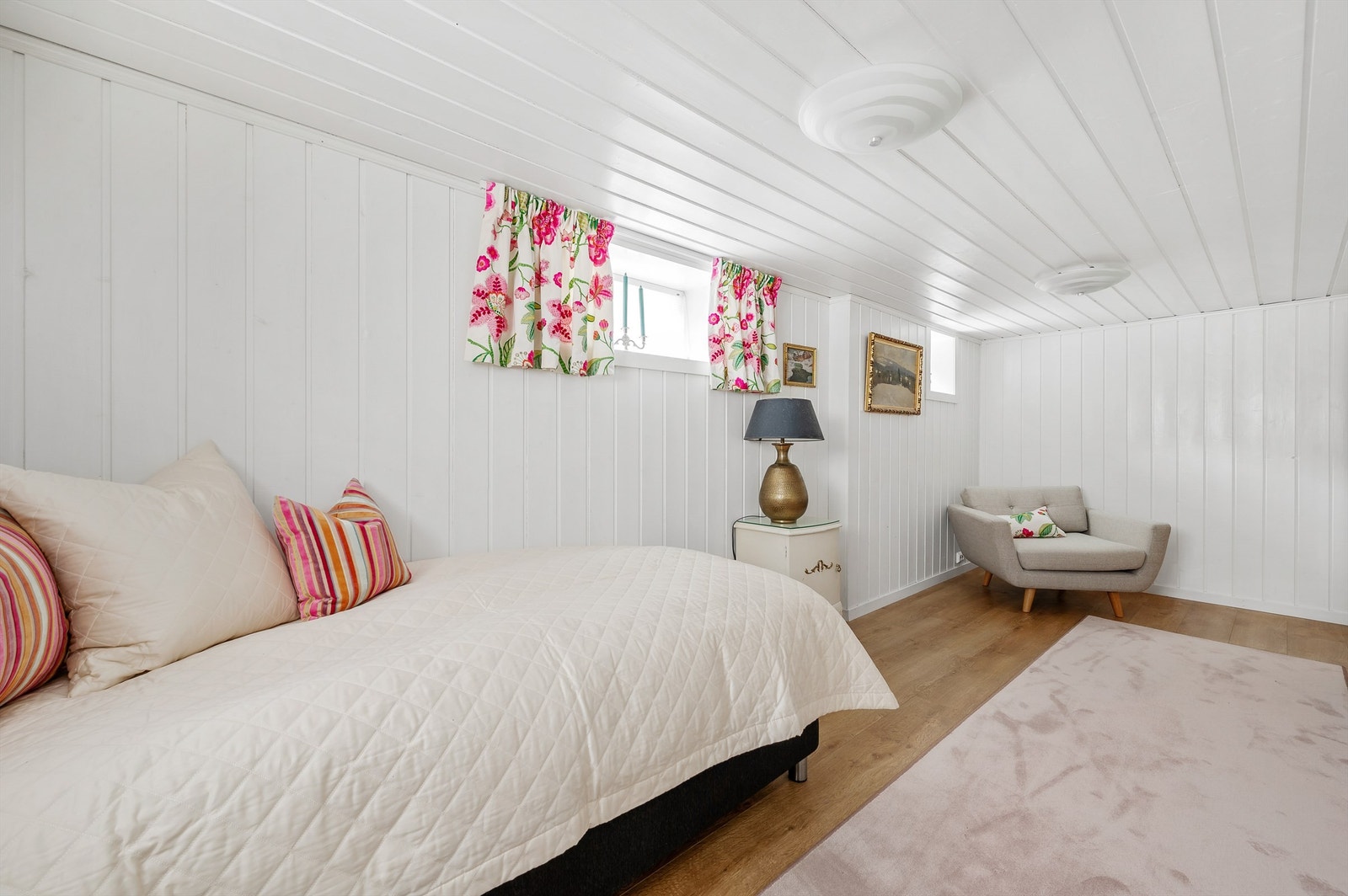 Soverommet er romslig med vinduer langs to sider, hvitmalte paneloverflater og enstavs gulv. Galleribilde