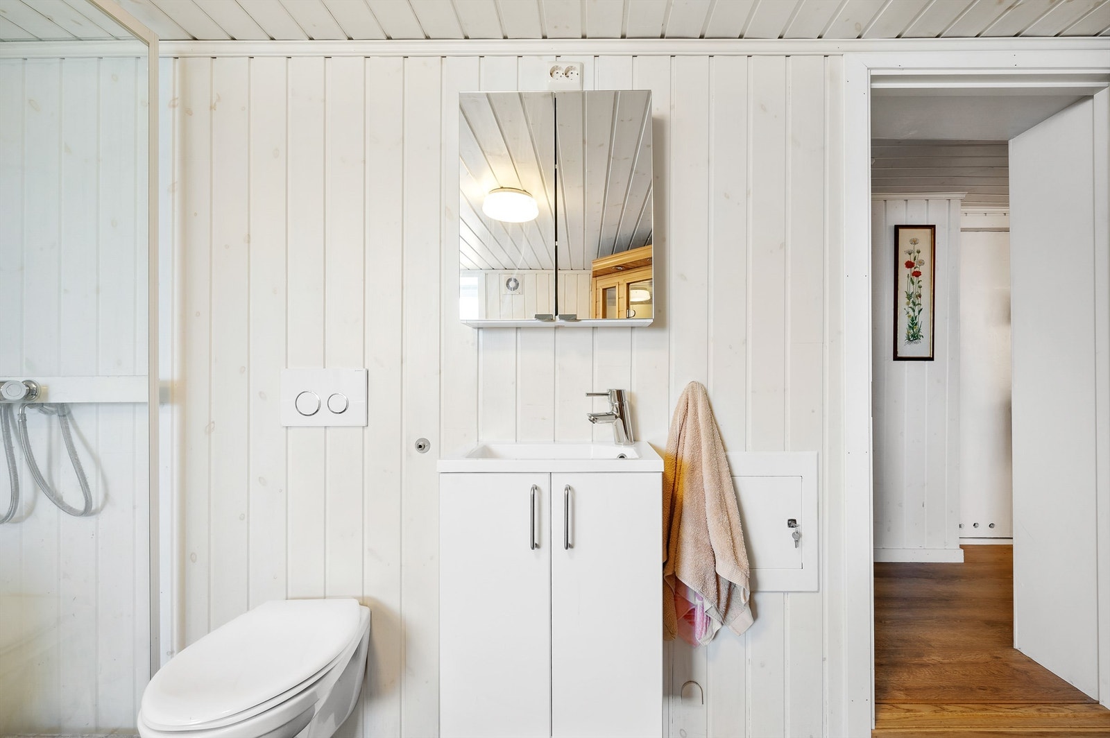 Badet er stort og pent utført med mørke fliser på gulvet, gulvvarme, samt lysmalte vegger og tak i panel. Videre er det et dusjkabinett, et veggmontert toalett, en hvit servantinnredning og speilskap Galleribilde