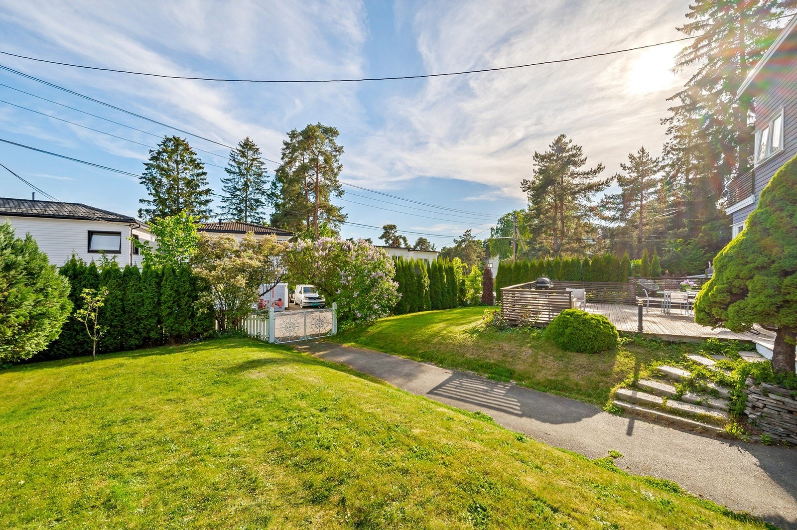 Tomten skjermes godt av høye furutrær, løvtrær, frodige prydbusker og blomstrende syriner. Galleribilde