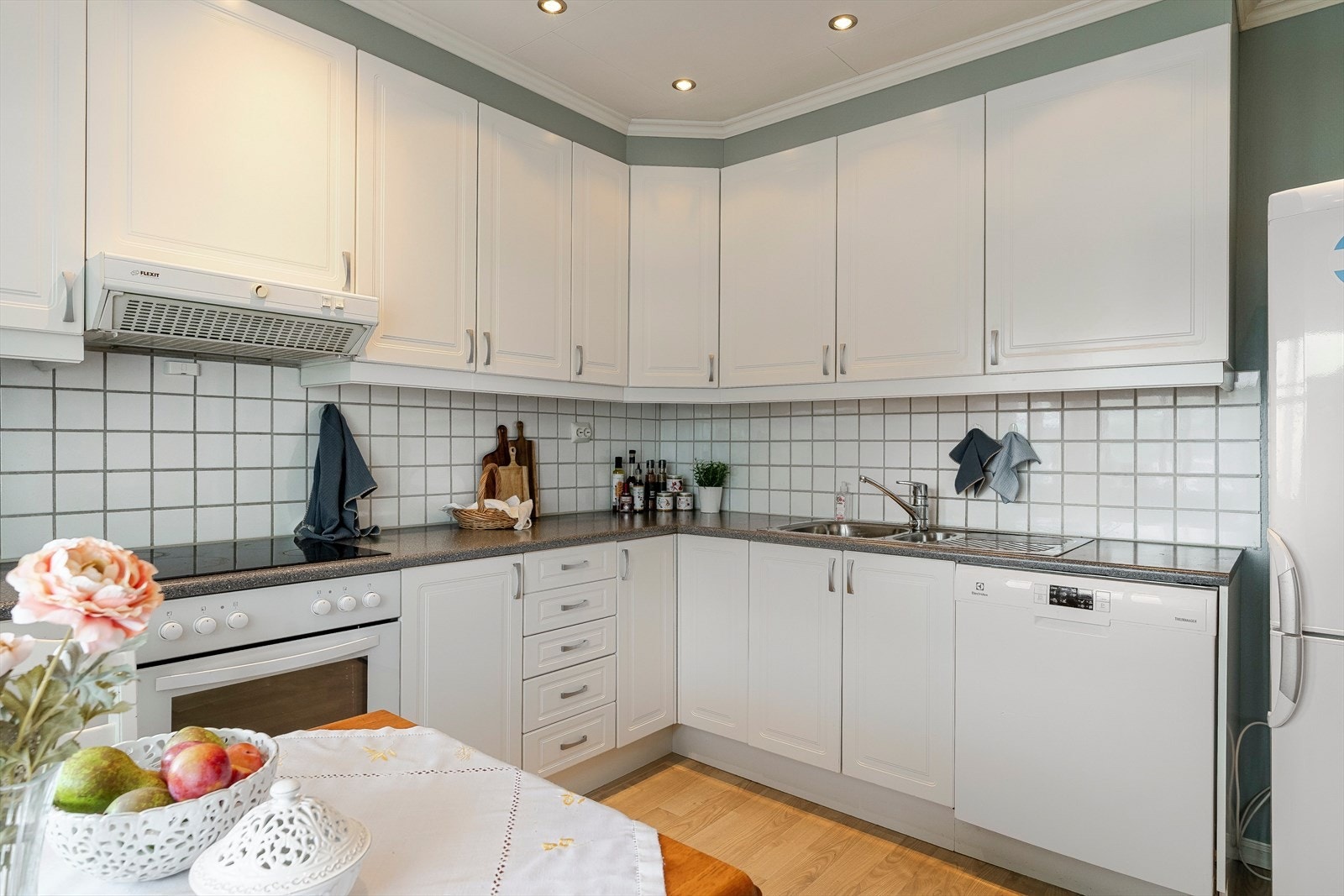 Innredningen har hvite profilerte fronter, vitrineskap og laminert benkeplate med dobbel oppvaskkum. Galleribilde