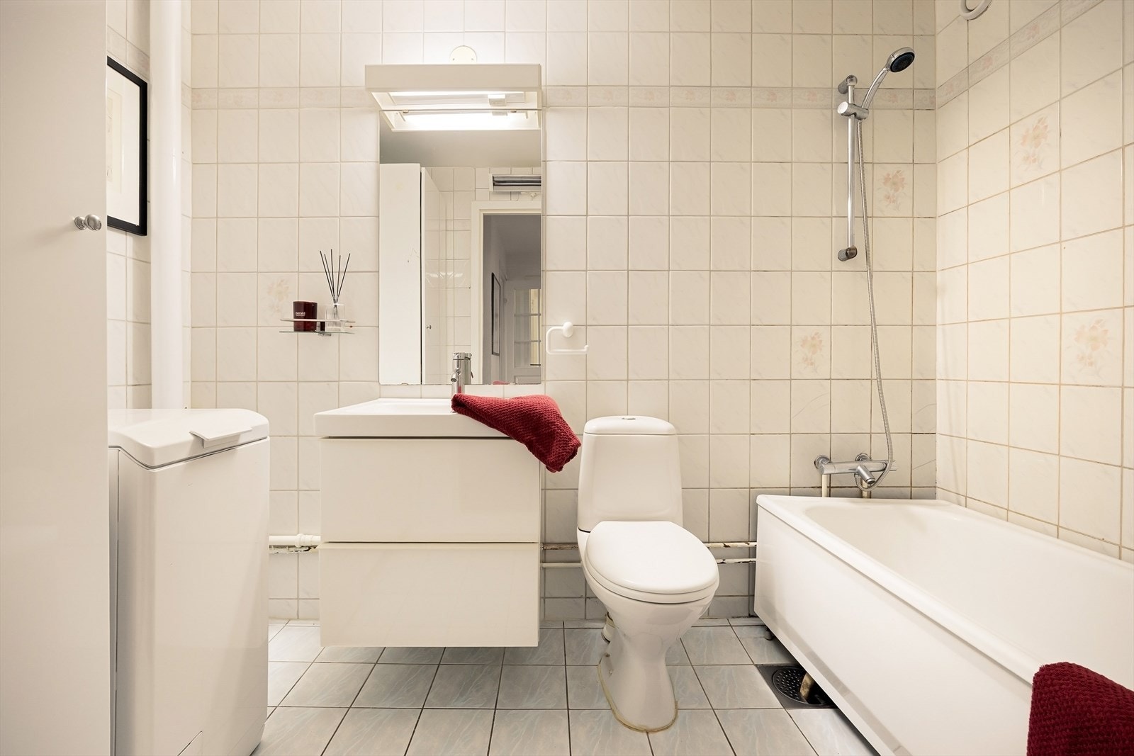 Lyst flislagt baderom med toalett, badekar og servant med innredning. Galleribilde