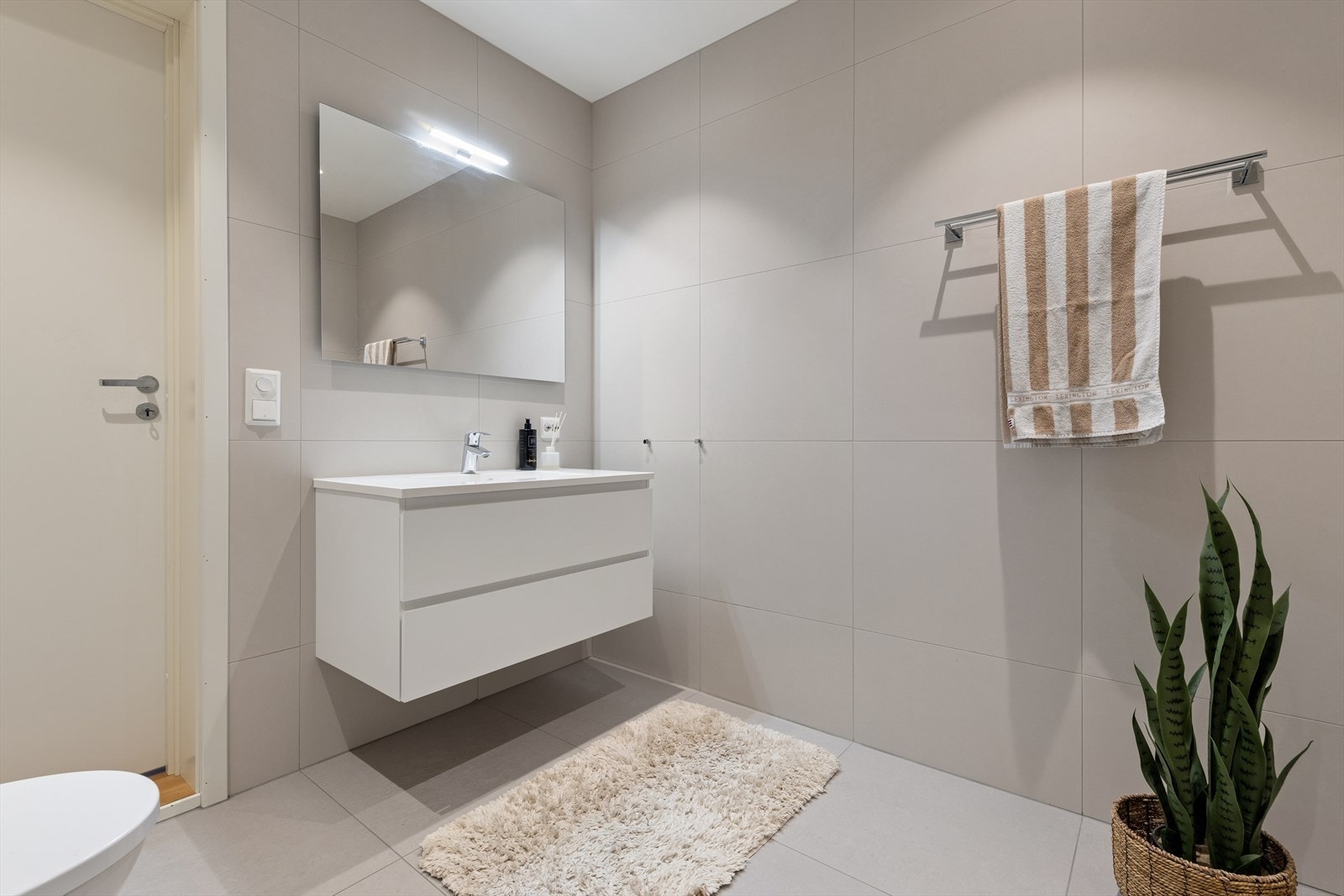 Baderommet i første etasje er innredet i tilsvarende stil som det andre badet og utstyrt med dusjhjørne, vegghengt toalett og baderomsinnredning med nedfelt servant. Galleribilde