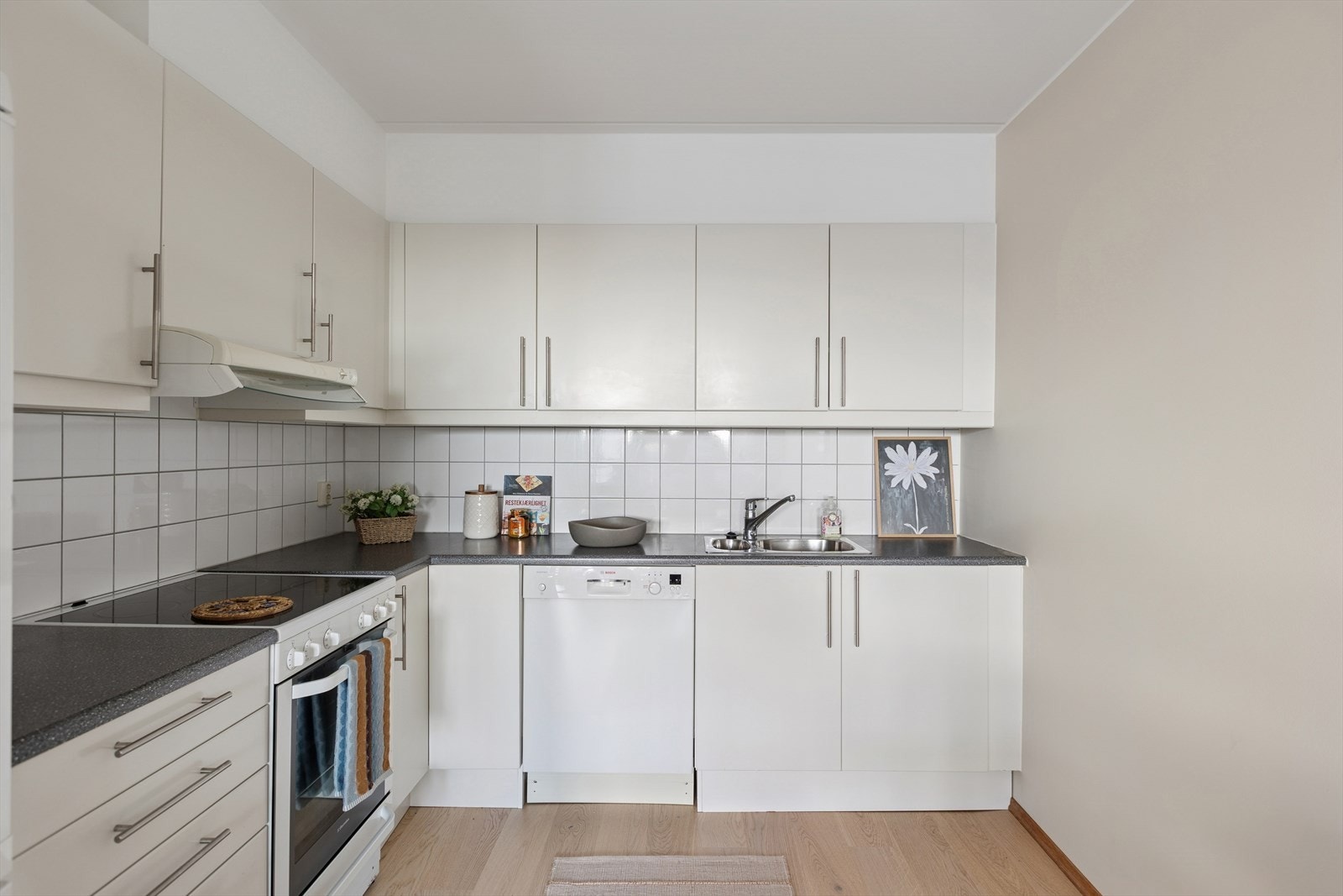 Det er en hvit kjøkkeninnredning med slette fronter, benkeplate i laminat og fliser over benk. Galleribilde