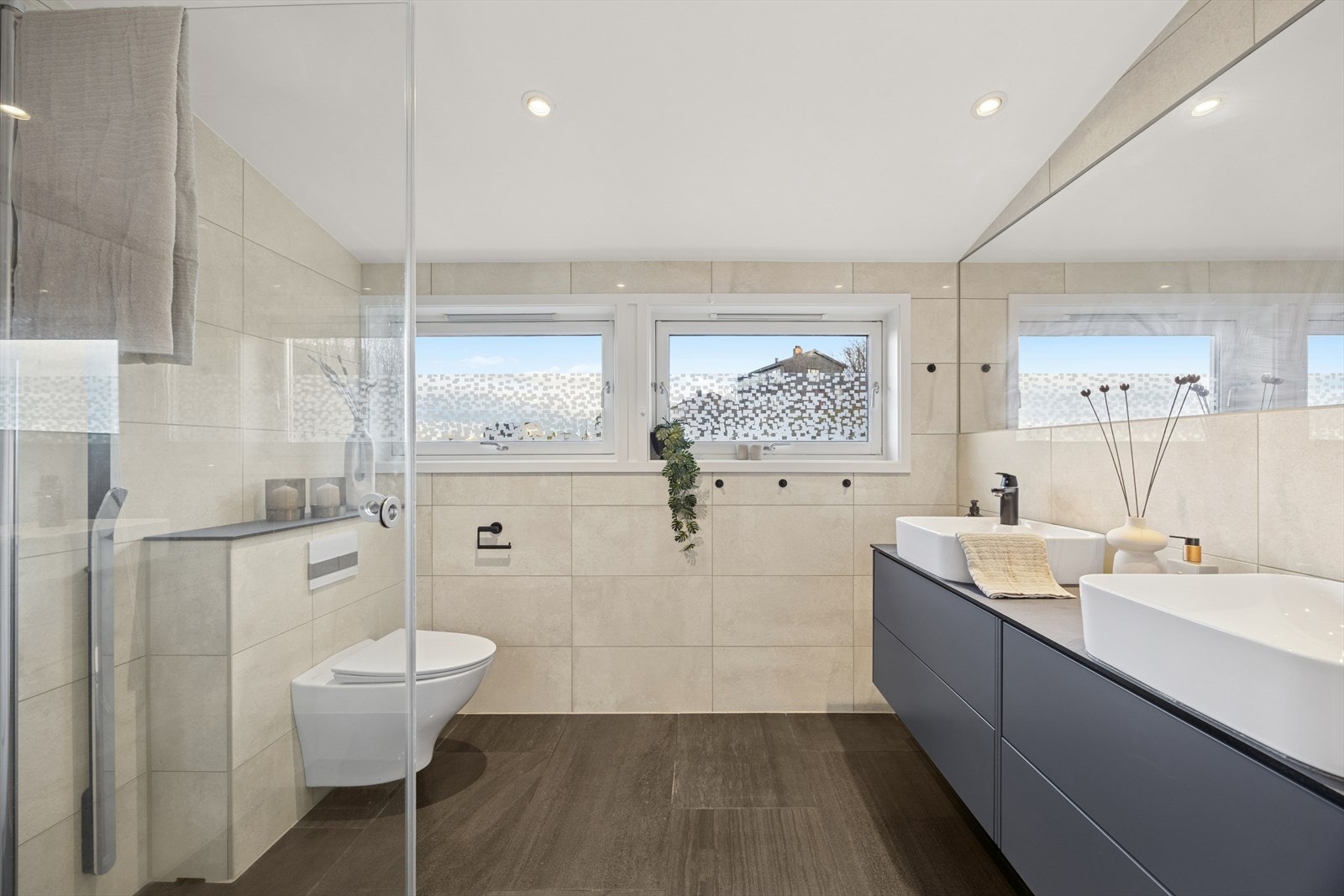 Flislagt baderom med behagelig gulvvarme fra 2016/17 utstyrt med veggmontert toalett med innebygd sisterne, dusjhjørne med dusjvegger, samt baderomsinnredning med to servanter og stort veggspeil. Galleribilde