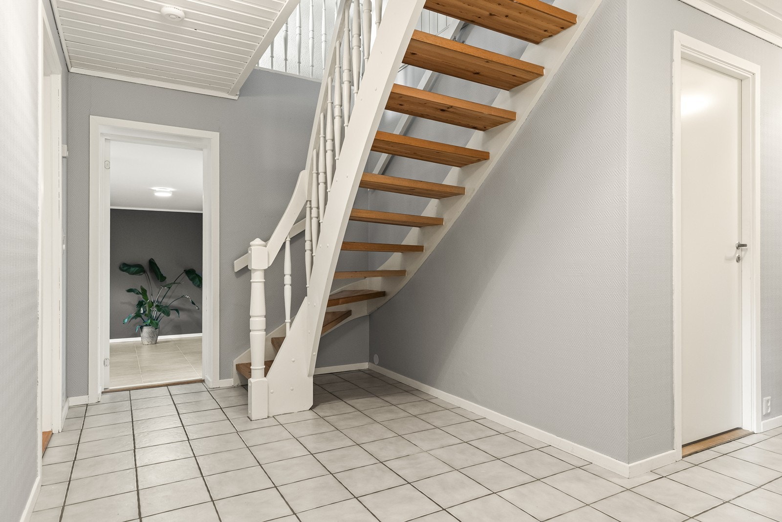 Tretrappen leder ned til en flislagt gang i kjelleren med adkomst til flere rom. Galleribilde