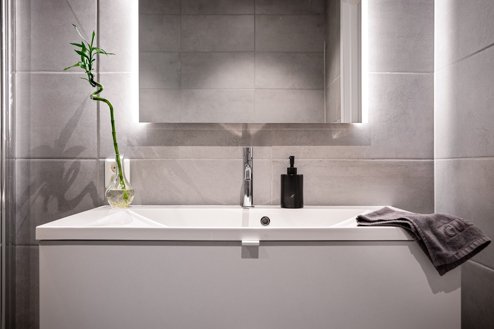 Badet er selvsagt helfliset og inneholder vegghengt toalett, helstøpt servant, skuffer under servant med slette fronter og dusjdører i klart glass. Galleribilde