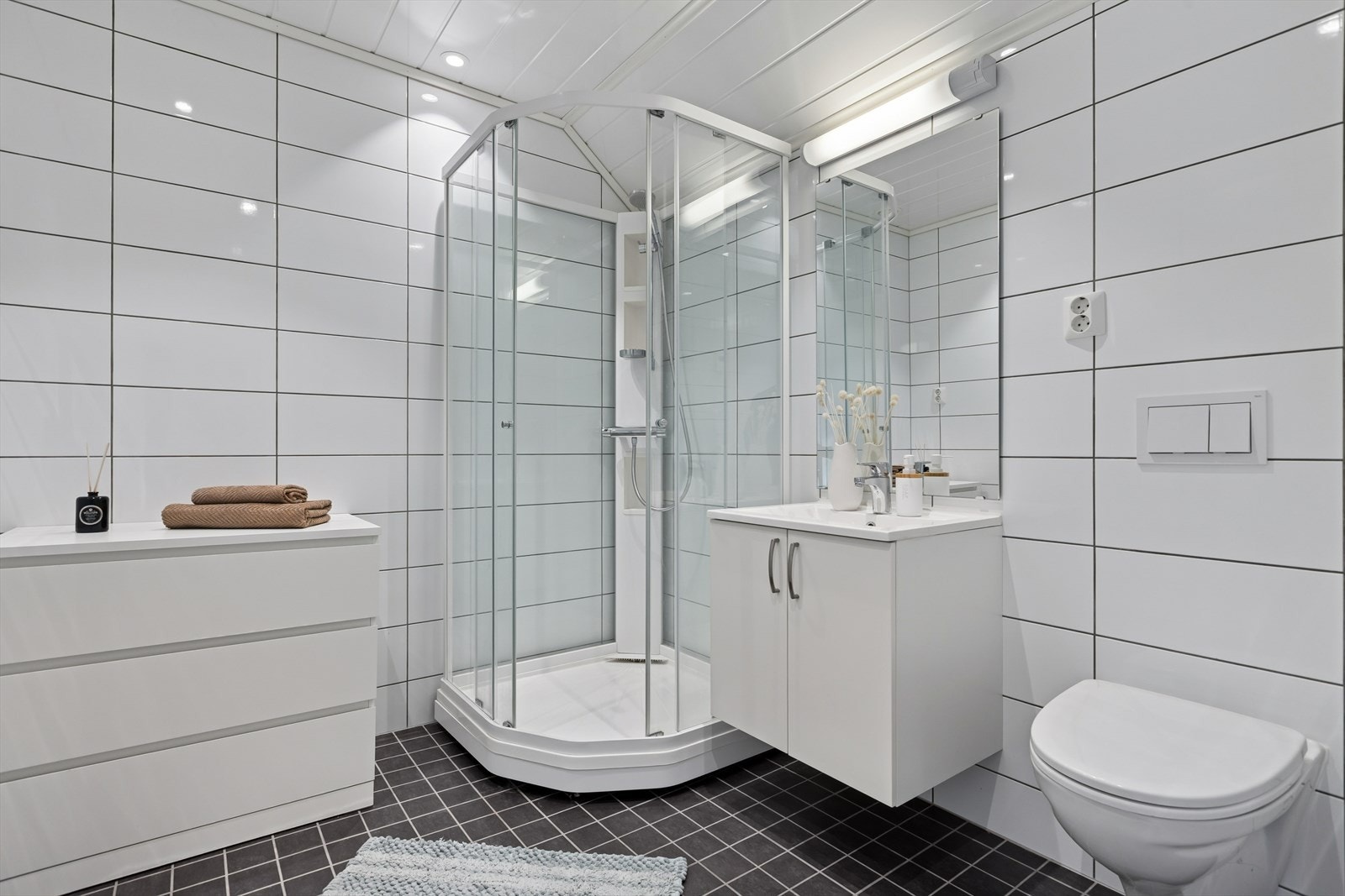 Lyst og flislagt baderom på loft utstyrt med dusjkabinett, vegghengt toalett og innredning med servant. Galleribilde