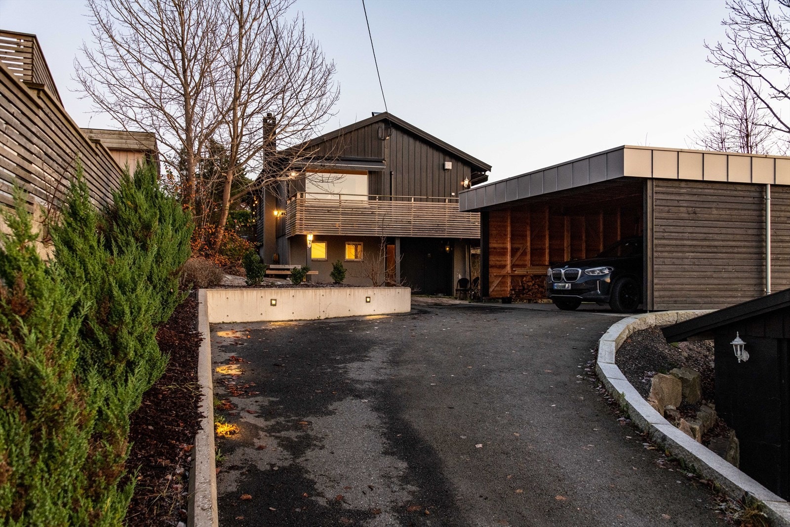 Innkjørsel til boligen har varmekabler, så slipper du å måke snø eller is på vinteren. Flott belysning langs støttemuren. Carport av nyere dato. Her er det enkelt å montere garasjeporter dersom det er ønskelig Galleribilde