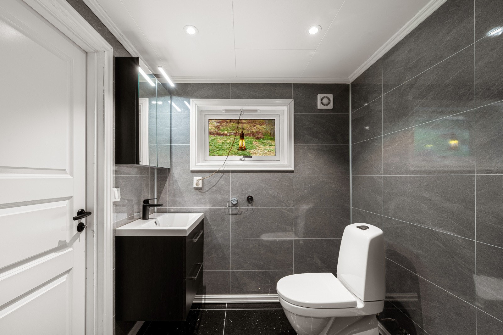 Badet er innredet med heldekkende servant, speilskap, gulvstående toalett og dusjhjørne med innfellbare dører i herdet glass. Galleribilde