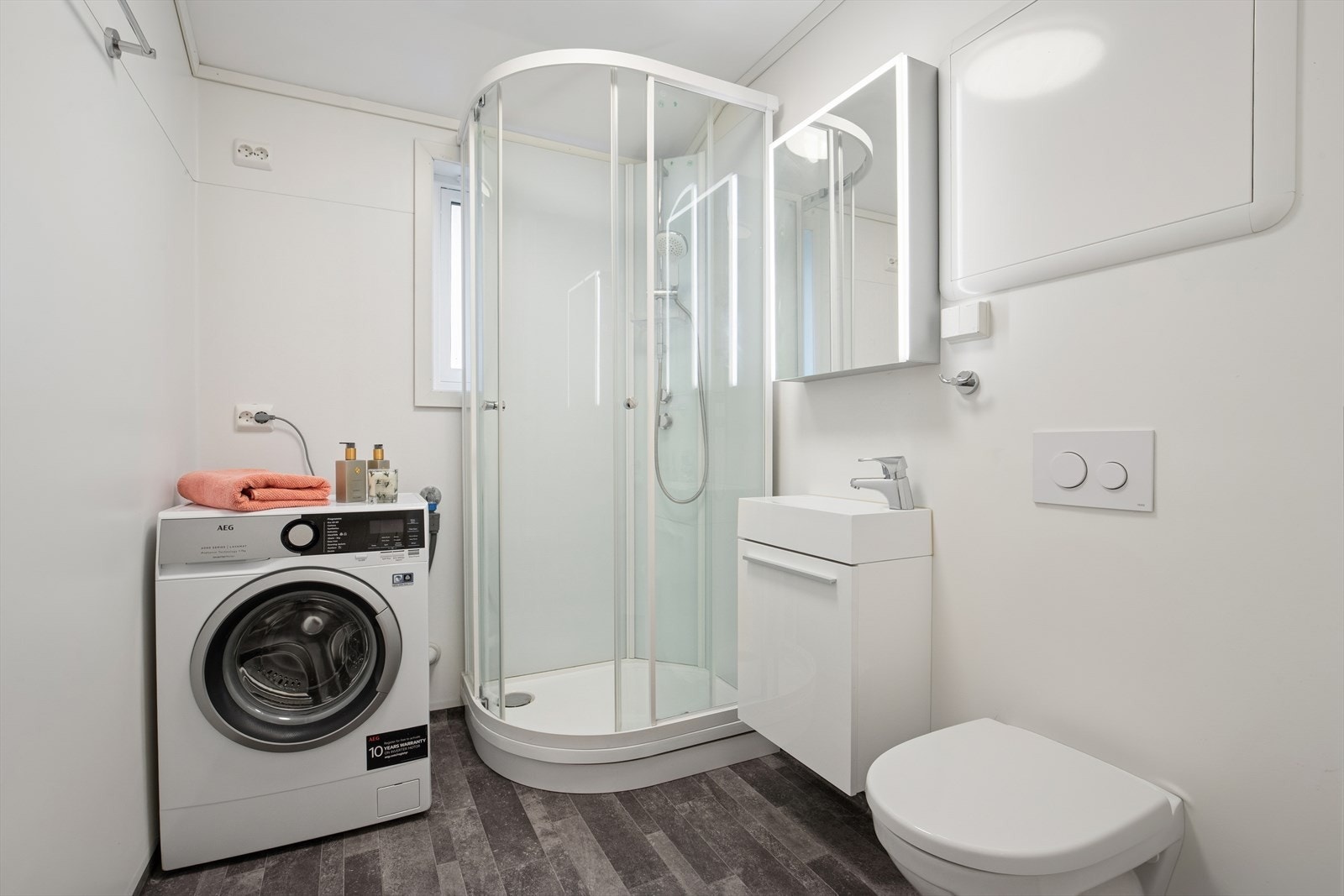 I likhet med kjøkken ble også badet oppgradert i 2021. Rommet har vinylbelegg på vegger og gulv, samt malt tak. Rommet er innredet med sanitærutstyr som servant med underskap, speil med belysning, vegghengt toalett, dusjkabinett og opplegg for vaskemaskin Galleribilde