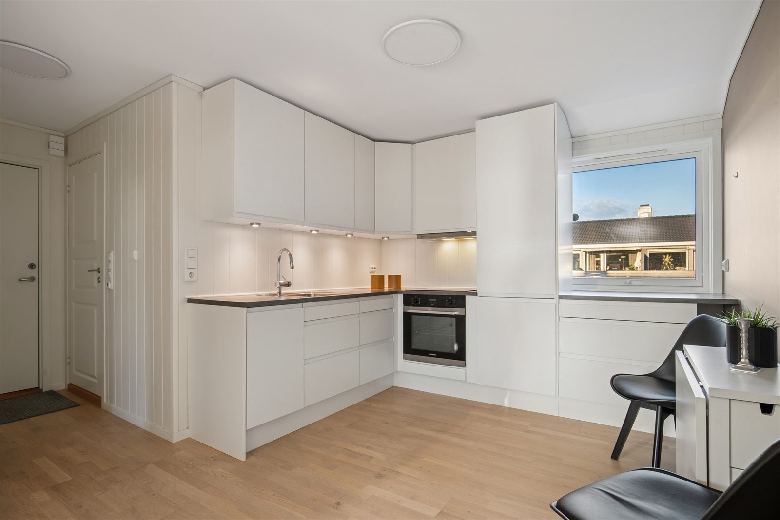 Kjøkkenet fra 2021 har en innredning med hvite, slette fronter og en mørk benkeplate. Galleribilde