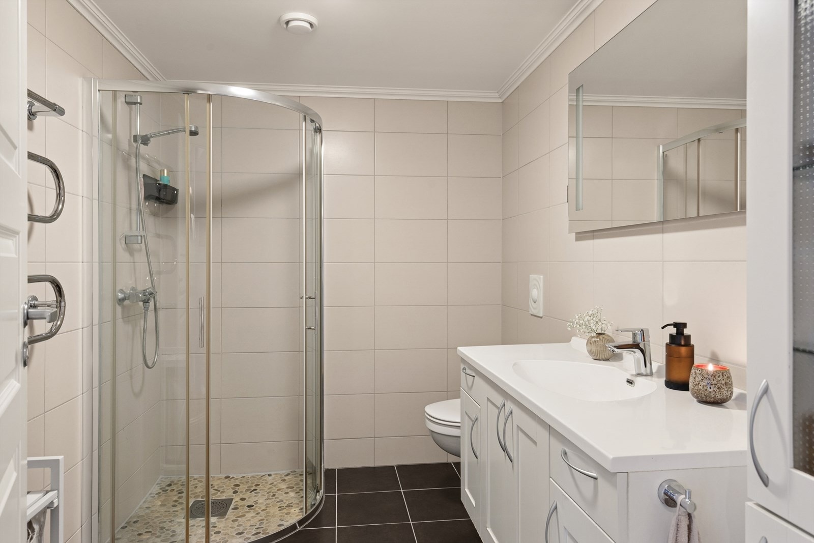 Rommet er innredet med en baderomsinnredning med servant, et veggmontert toalett og et dusjhjørne. Galleribilde