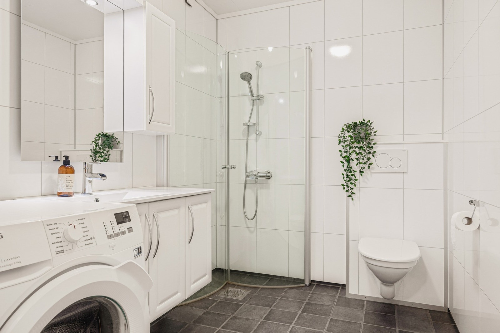 Badet er innredet med dusj m/glassvegger, vegghengt toalett, baderomsinnredning og opplegg for vaskemaskin. Galleribilde