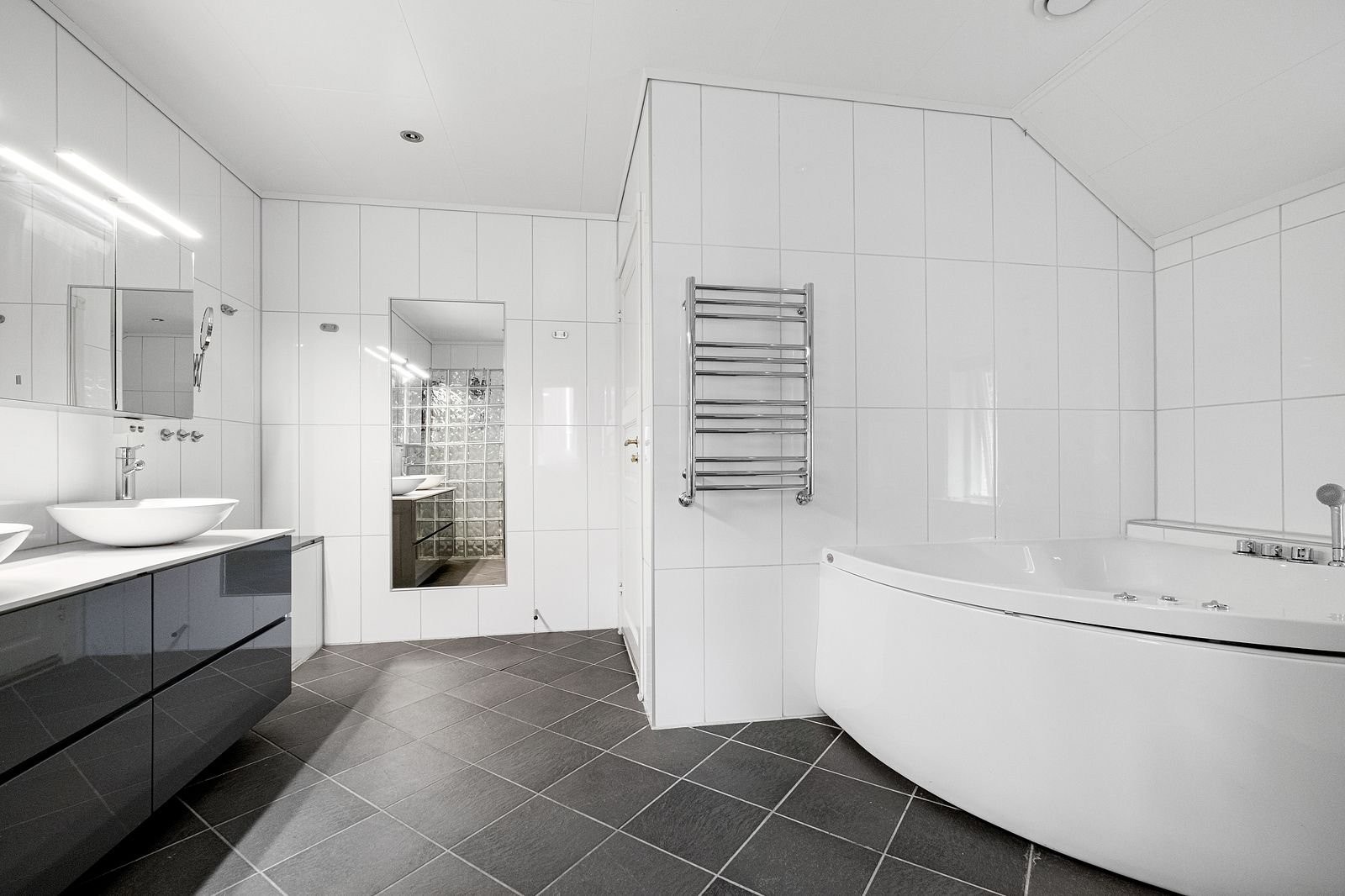 Rommet er innredet med innredning med 2 nedfelte servanter, veggmontert toalett, badekar og dusjvegger/hjørne Galleribilde