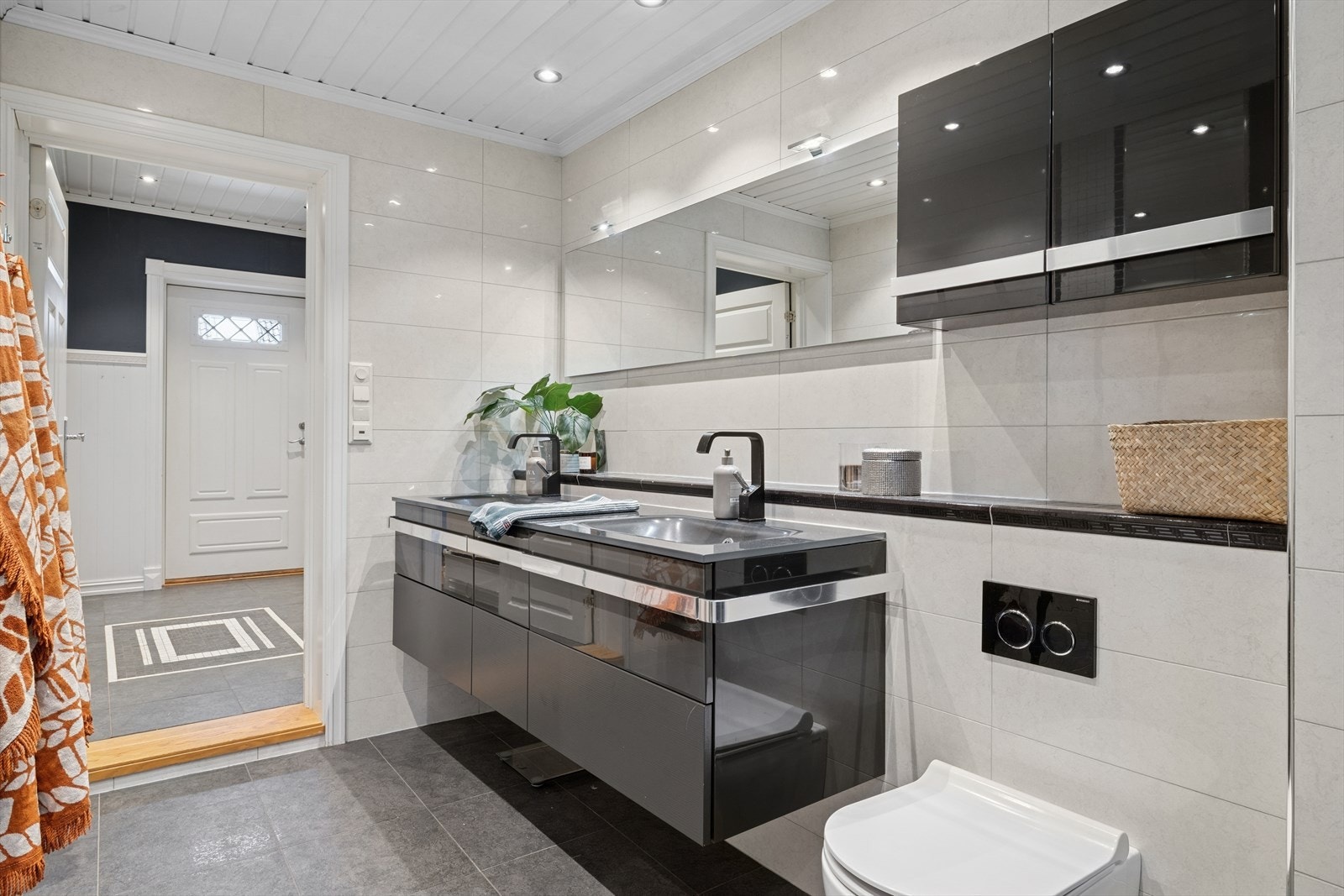 Badet har et dusjhjørne med innfellbare dører i herdet glass, to servanter i helstøpt plate, veggfestet klosett med innebygget sisterne og opplegg for vaskemaskin. Galleribilde