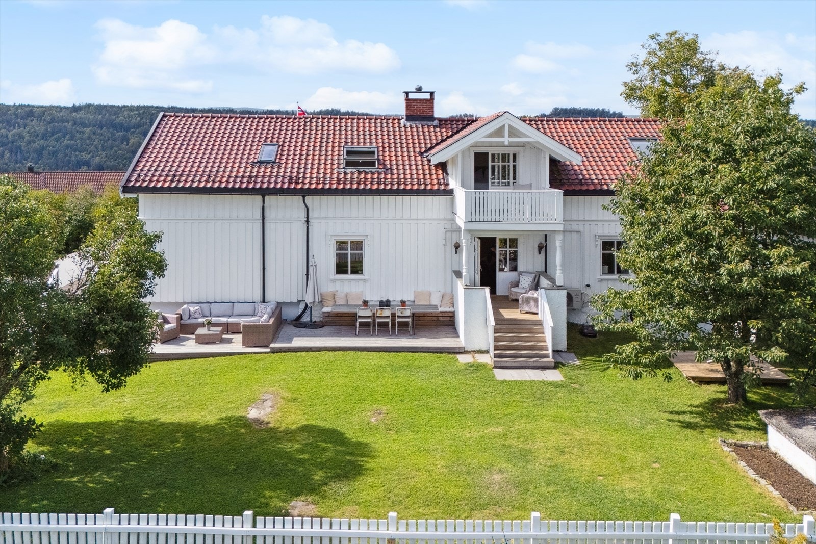 Tomten er relativt flat, pent opparbeidet og velstelt med plen, beplantning og steinsatt biloppstillingsplass for flere biler ved garasje. Galleribilde