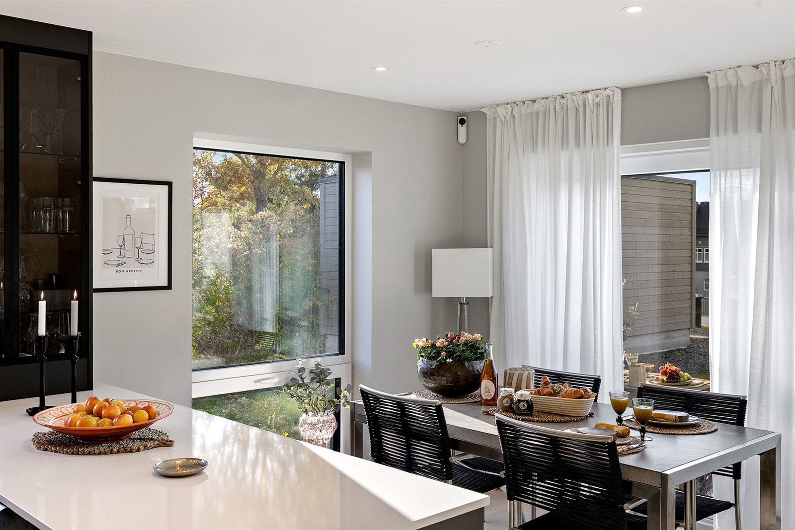 Kjøkkenet har integrerte hvitevarer fra Elektrolux og Bosch, praktisk belysning under overskapene og et elegant vitrineskap med glassdører. Sorte detaljer på armatur, håndtak og hvitevarer gir en helhetlig og eksklusiv stil. Galleribilde