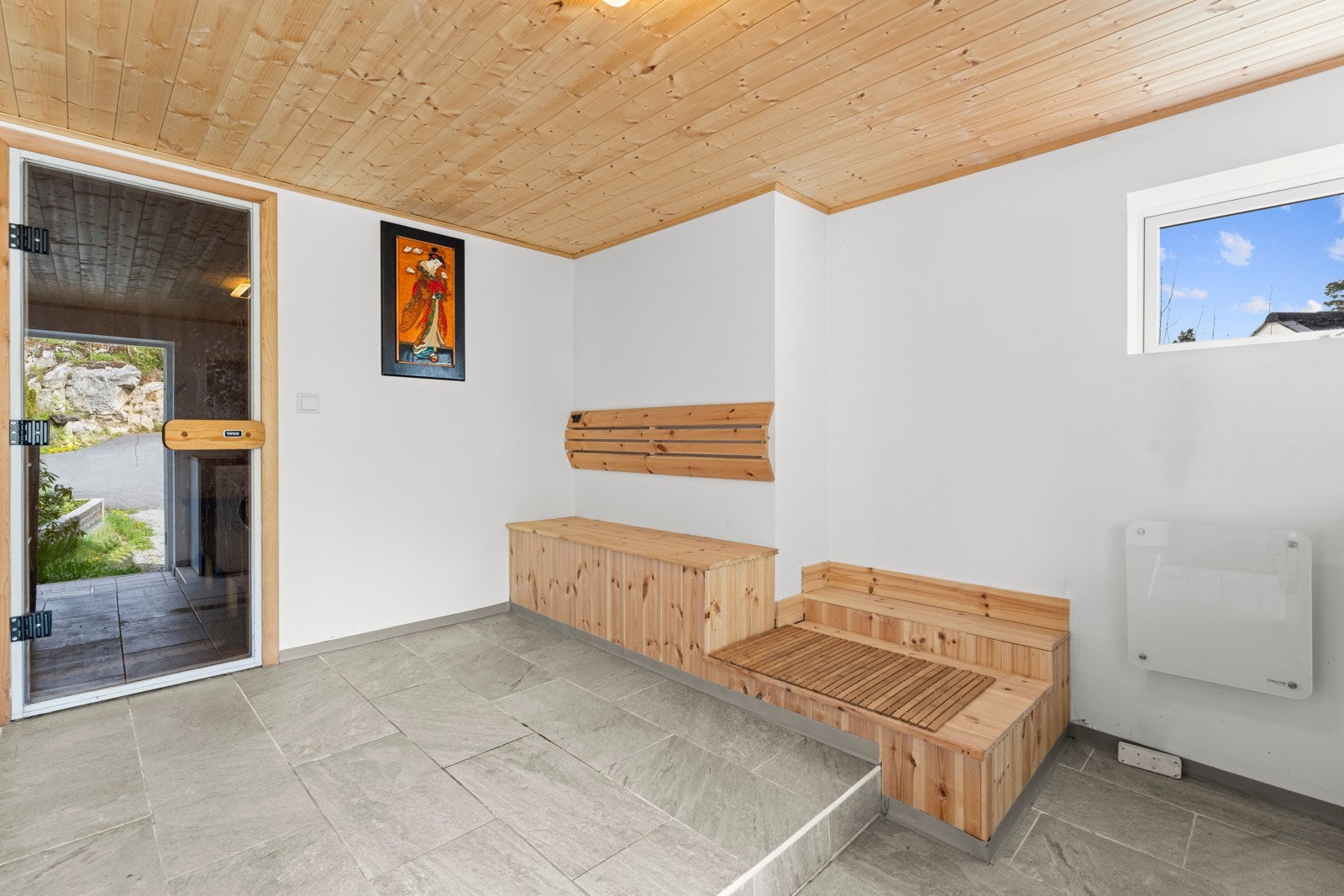 Kjellerrommet har hvitmalte vegger og lysegrå gulvfliser, og langs ene veggen er det plassbygde sittebenker i heltre. Galleribilde