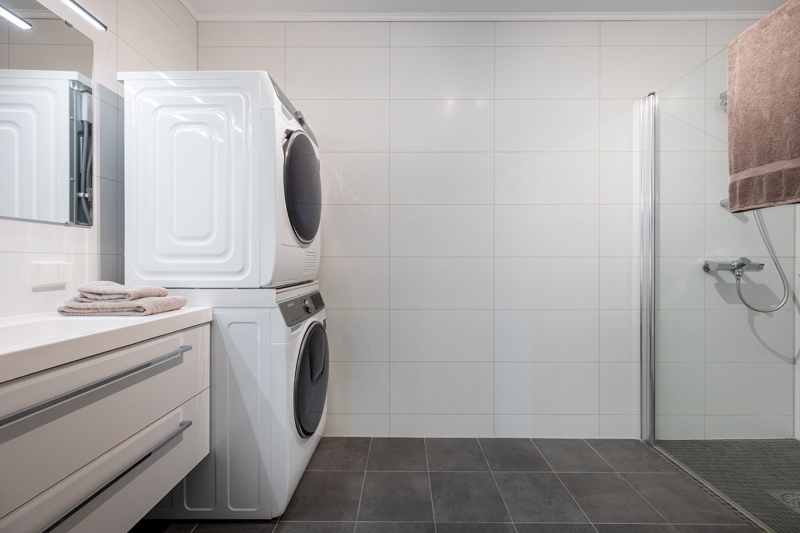 Første etasjes badeværelse holder en ren og behagelig standard med grå gulvfliser, hvite vegger og tak og mosaikk i dusjesonen. Galleribilde