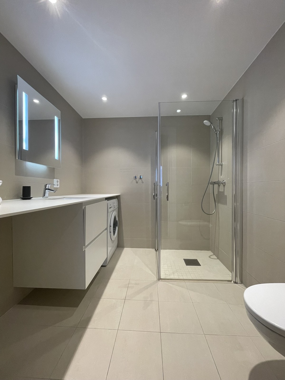 Lekkert flislagt bad med varme i gulv. Opplegg for vaskemaskin og tørketrommel Galleribilde