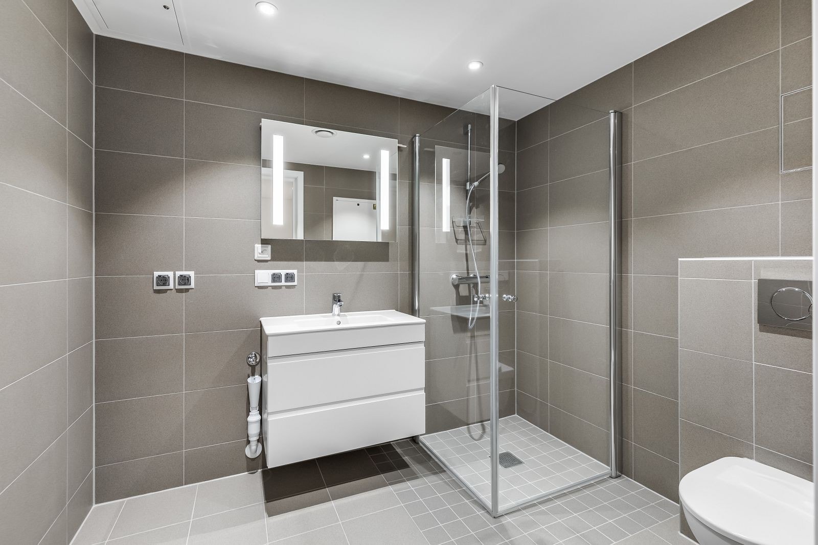 Lekkert flislagt bad med varmekabler, downlights og opplegg for vaskemaskin. Galleribilde