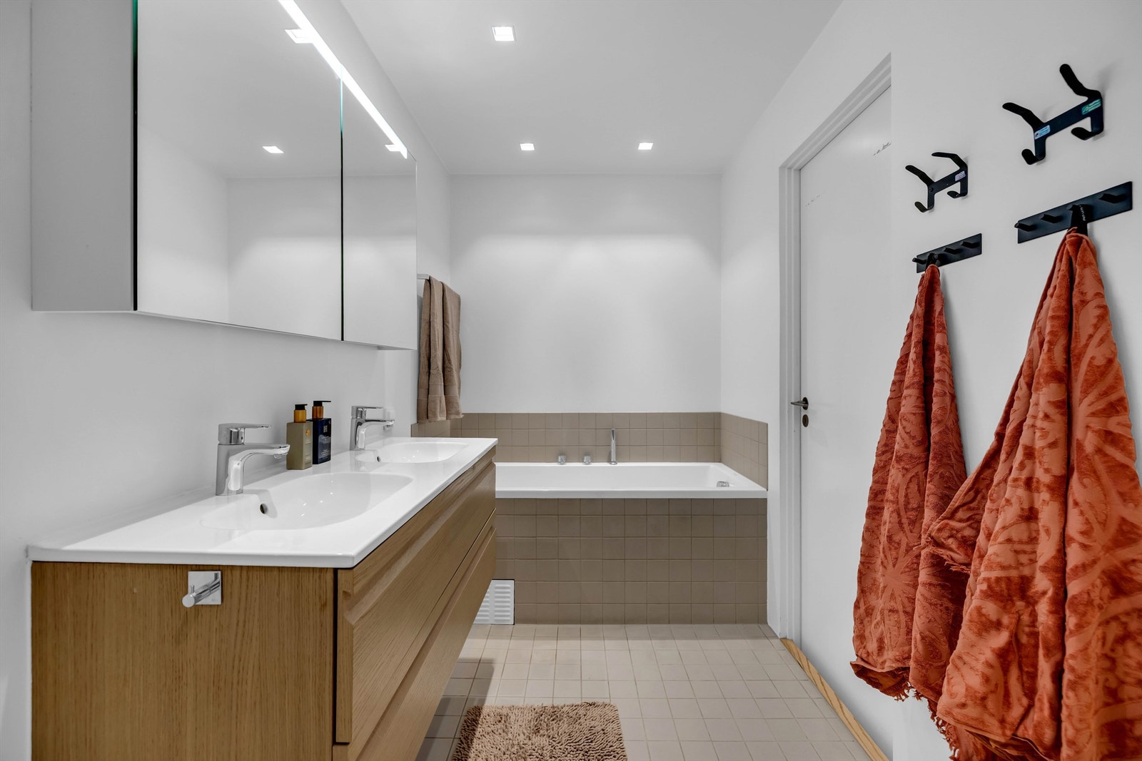 Rommet er flislagt med lun gulvvarmer og innredet med romslig dusjnisje, badekar, baderomsinnredning med skuffer og 2 nedfelte servanter, vegghengt toalett og stort speilskap Galleribilde