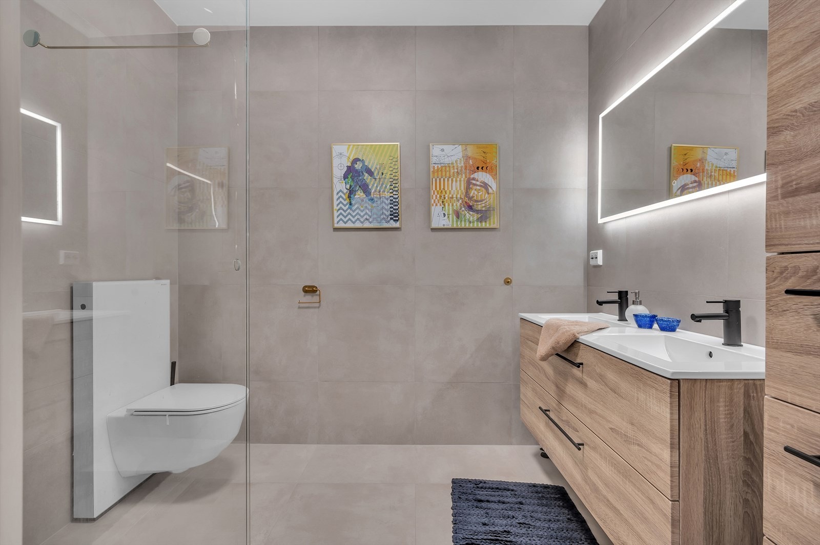 Lekkert bad med detaljer i sort og messing. Moderne, store fliser på gulv og vegger gir et godt inntrykk. Det er god oppbevaringsplass i dobbel servant og høyskap med plass til håndklær og utstyr. Galleribilde