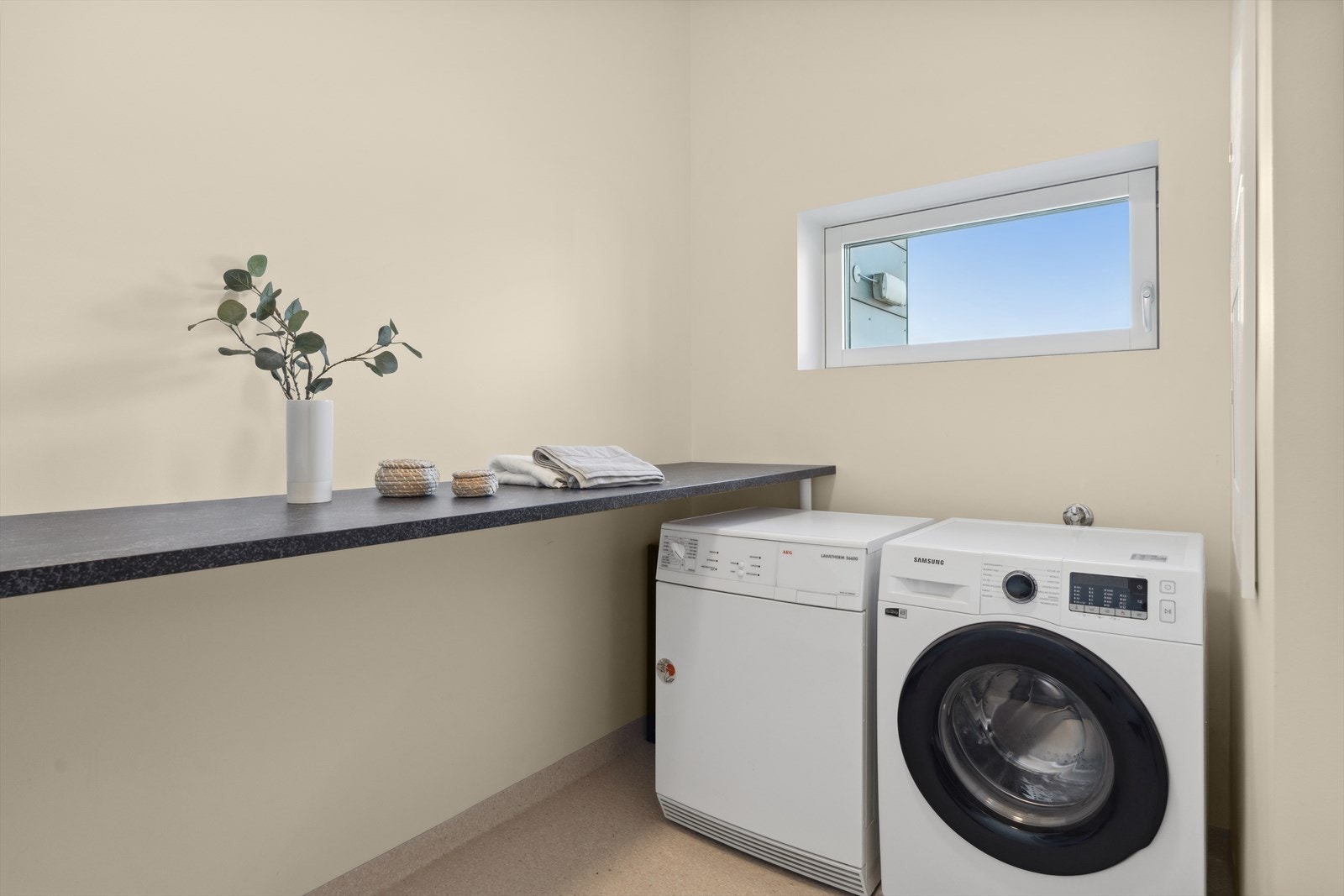 Separat vaskerom med belegg på gulvet og praktisk arbeidsbenk. Plass for vaskemaskin og tørketrommel. Galleribilde