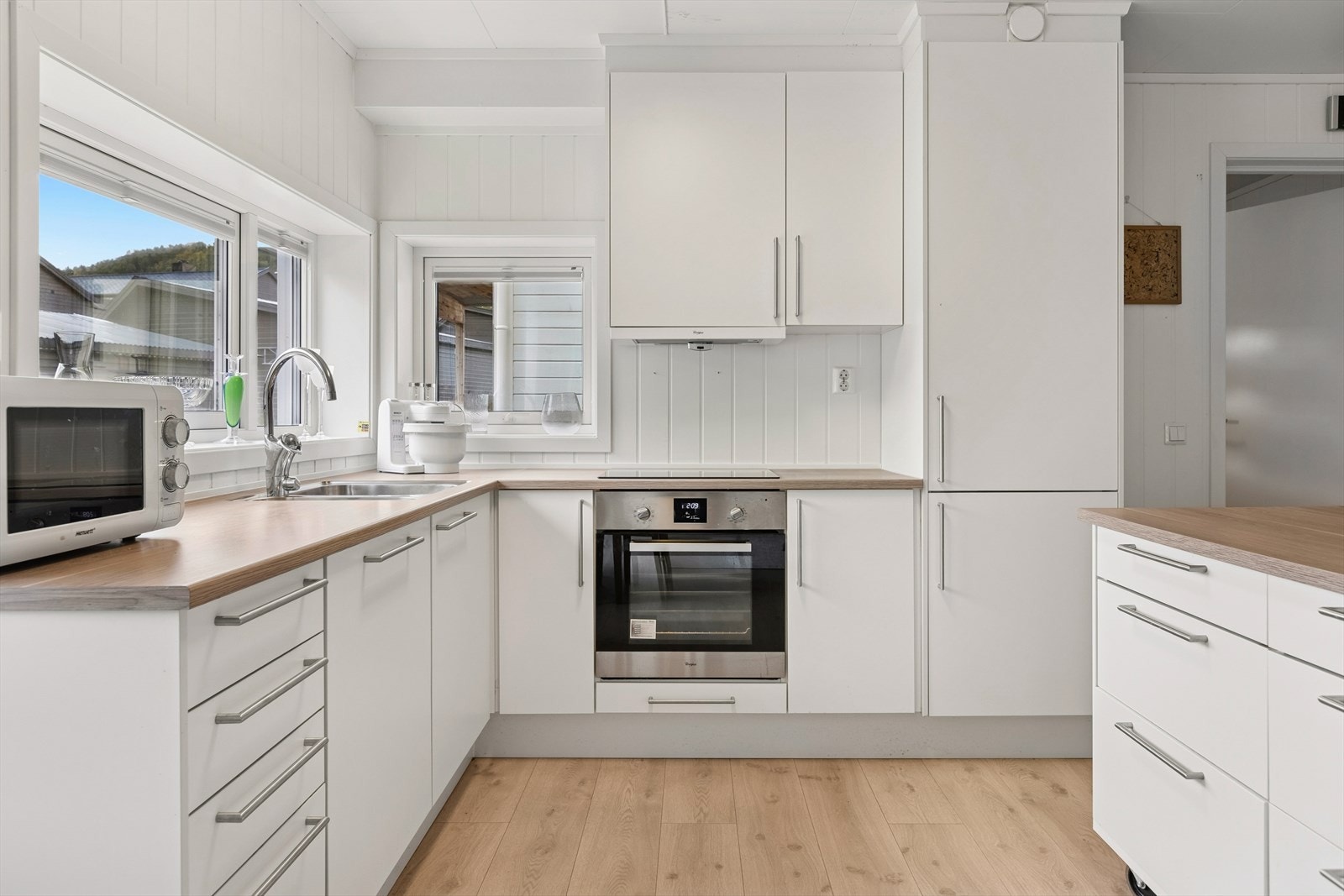 Tidløst hjørnekjøkken med slette fronter i lys utførelse. Kjøkkenet har en praktisk kjøkkenøy på hjul som gir fleksibilitet og kan enkelt flyttes etter behov. Galleribilde