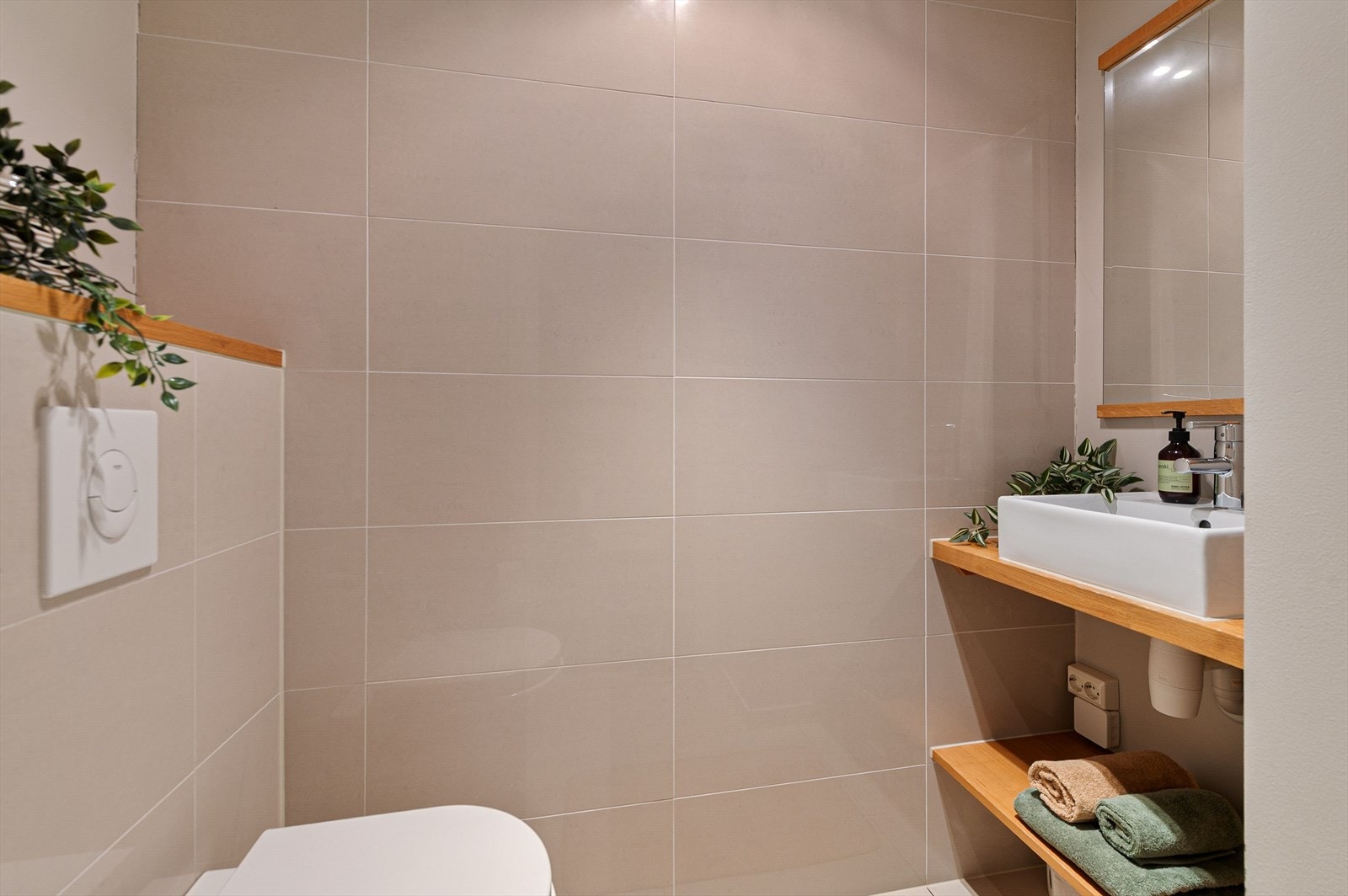 Gjestetoalett med plassbygget innredning med servant og speil. Vegghengt toalett og flislagte overflater. Galleribilde