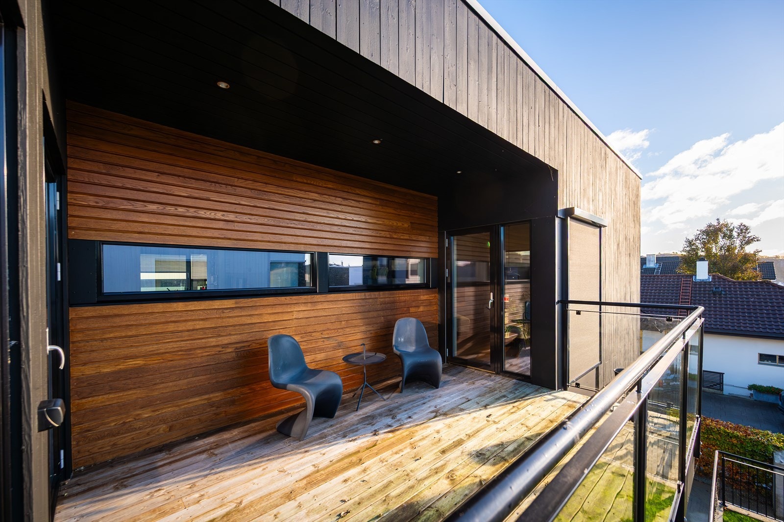 Balkong med trepanel og glassrekkverk gir en stilren ramme for utemøblering. Galleribilde