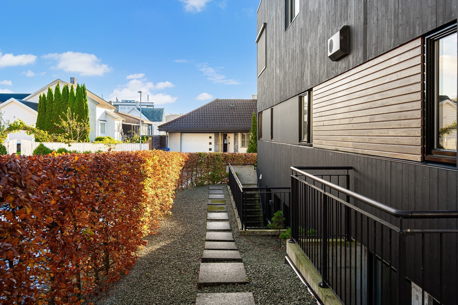 Gangvei langs huset med grusdekke og steinheller, omkranset av hekk. Galleribilde