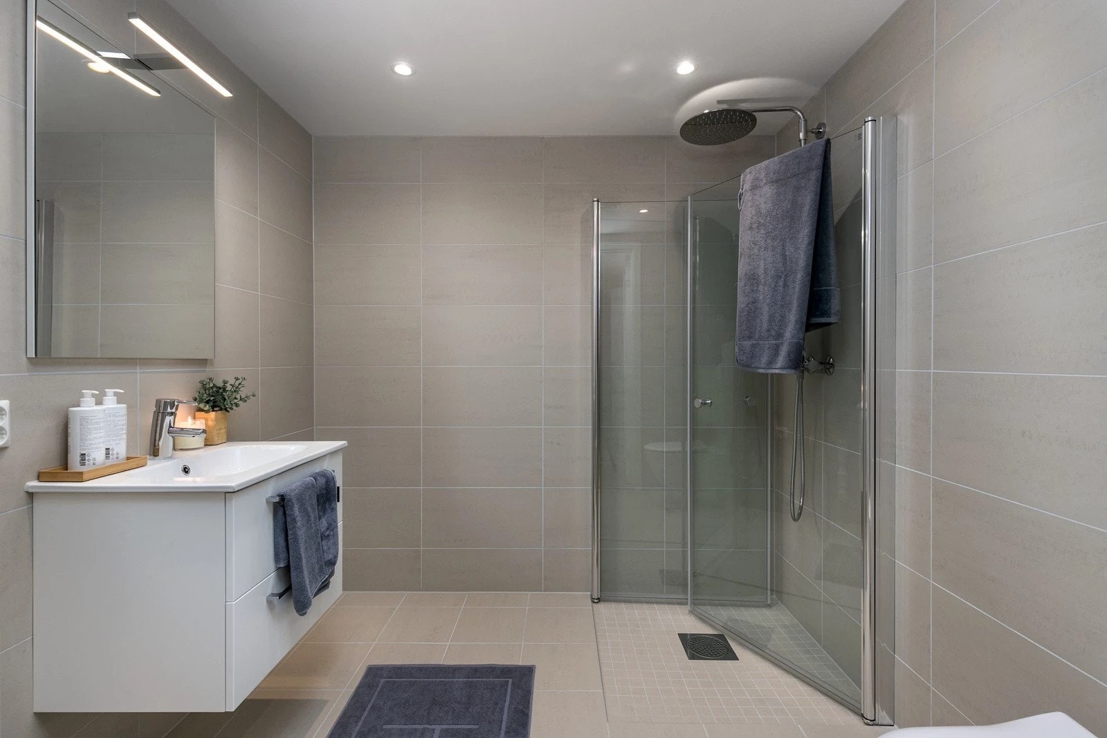 Delikate og baderom med sandfargede fliser, innfellbare dusjvegger og opplegg til vaskemaskin. Galleribilde