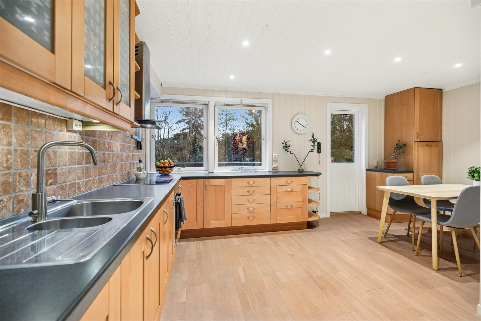 Kjøkkenet har en vinkelformet innredning fra Ikea med bjørkefronter, overskap med glassfelt og laminerte benkeplater. Galleribilde