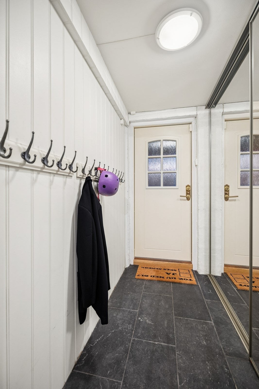 Egen inngang til boligens kjeller med plassbesparende skyvedørsløsning med speilfronter og praktiske knaggrekker for ekstra opphengsmuligheter. Galleribilde