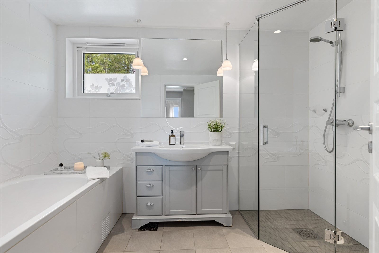 Pent, flislagt baderom utstyrt med servant, dusj og badekar. Galleribilde