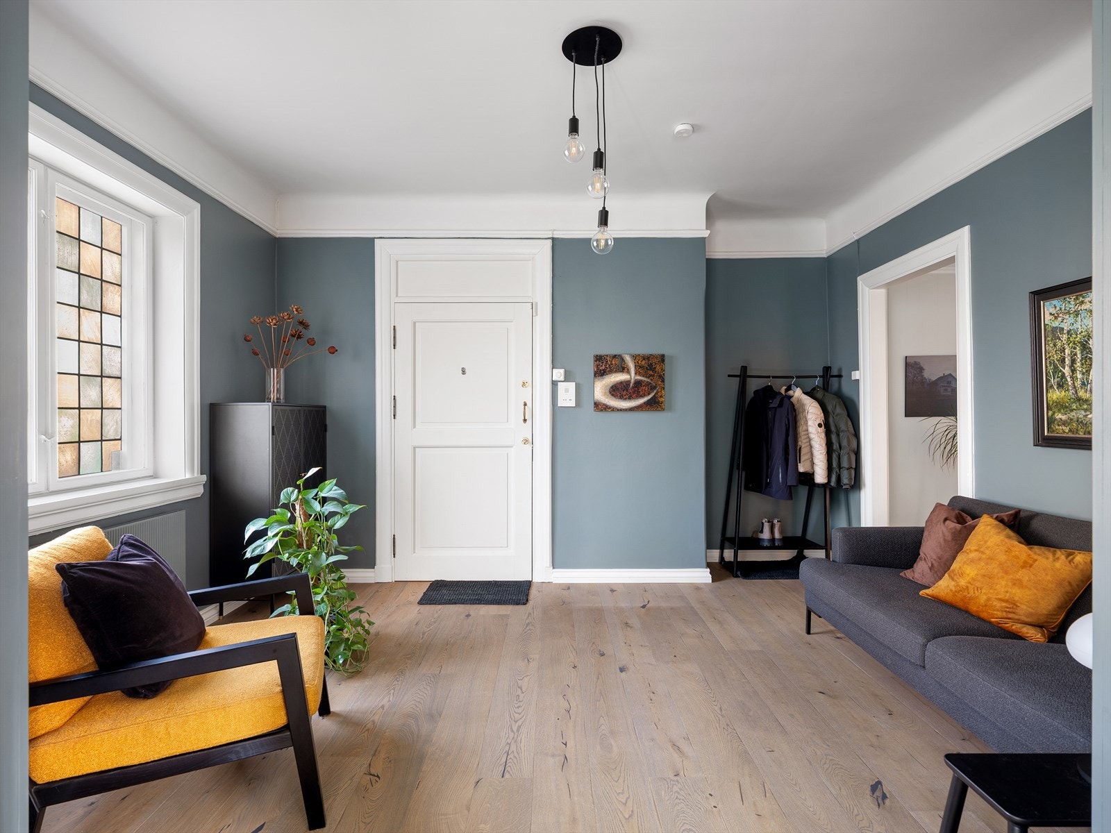 Stor hall med 1-stavs eikeparkett og antatt originalt vindu med farget glass. Inngangsdøren ble brannsikret i 2025 Galleribilde