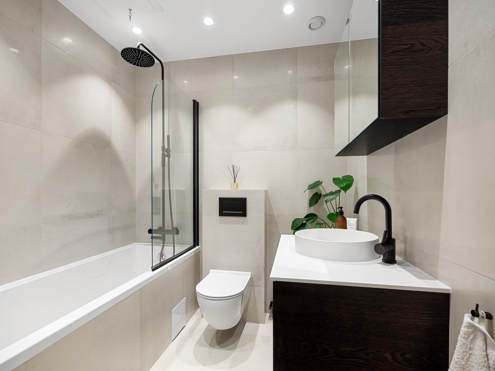 Delikat, helfliset bad med varmekabler i gulv, downlights i himling og badekar med regnfallsdusj Galleribilde