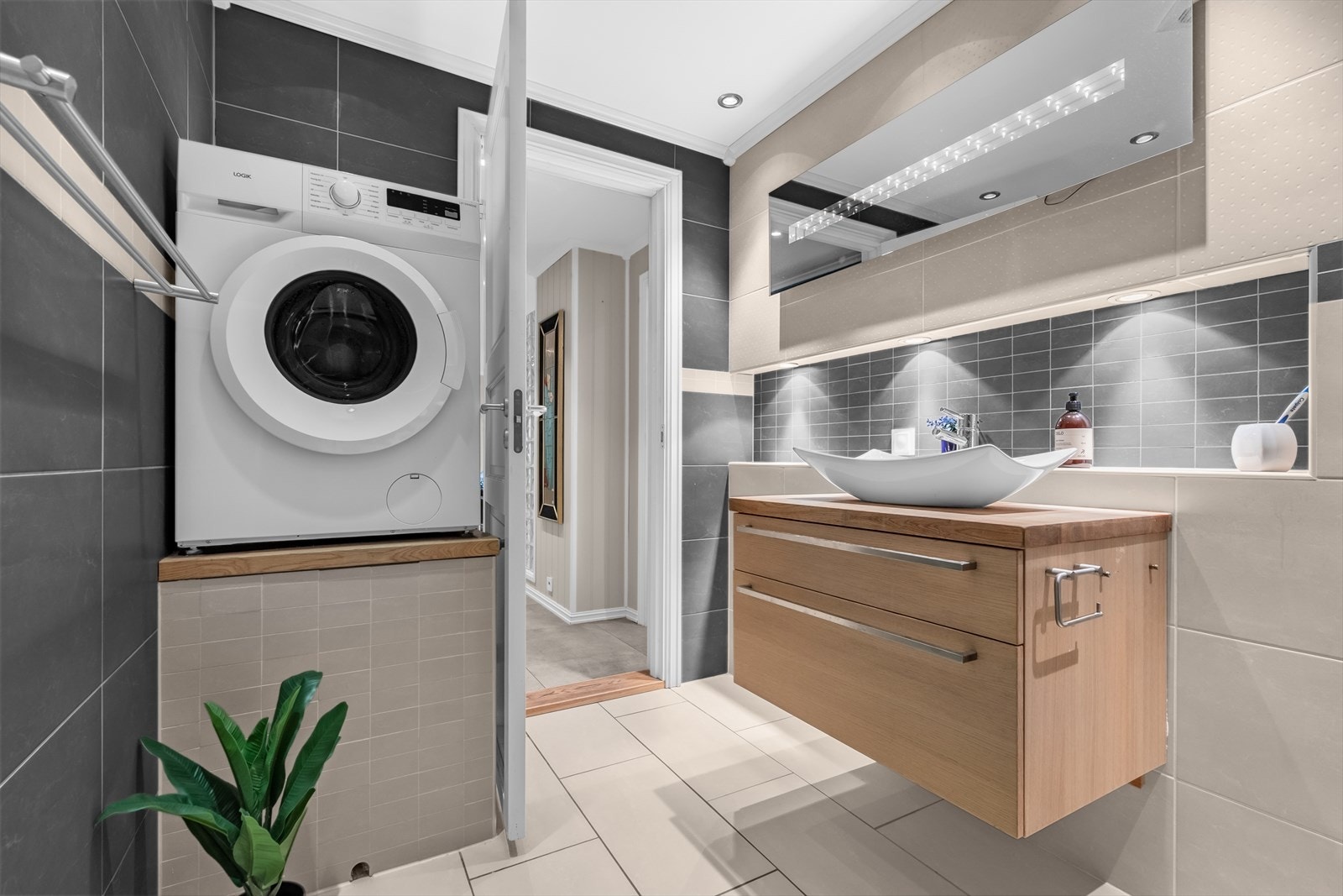 Rommet er utstyrt med innfellbare dusjdører, mekanisk periodisk avtrekk, opplegg for vaskemaskin, rørfordelingsskap, varmtvannsbereder, veggmontert wc og servantskap med ett-greps blandebatteri. Galleribilde