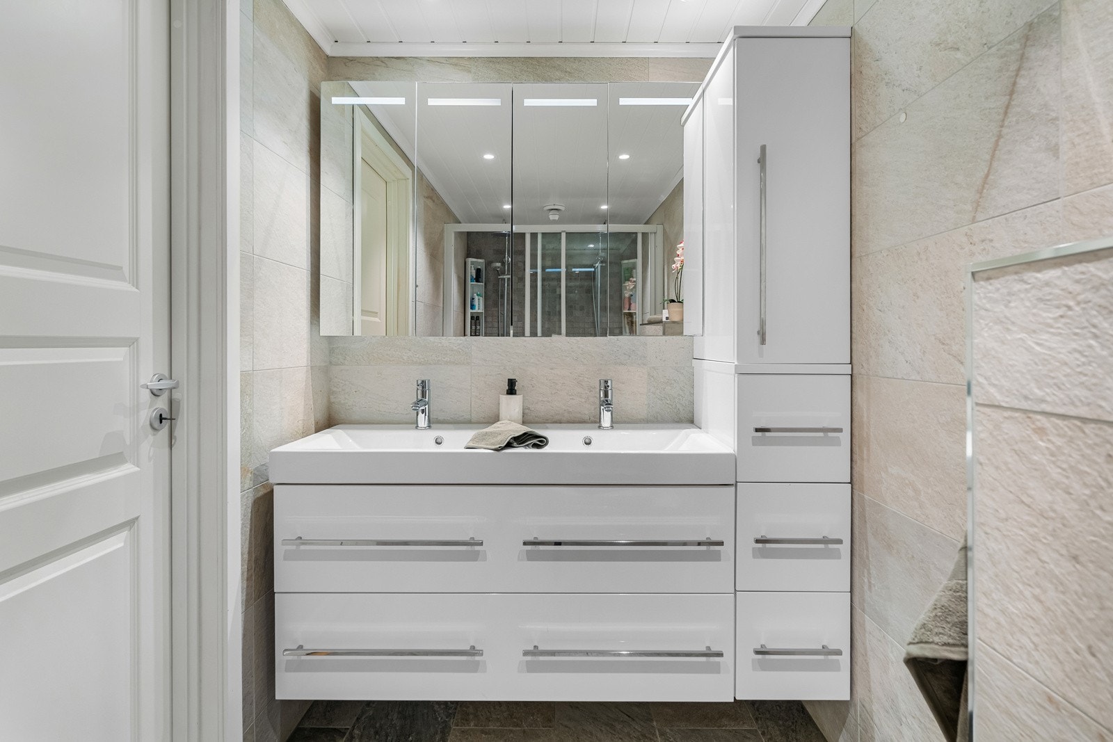 Baderomsinnredning bestående av benkeskap og veggskap med glatte fronter i høyglanset utførelse, samt veggskap med speil og belysning over servant. Galleribilde