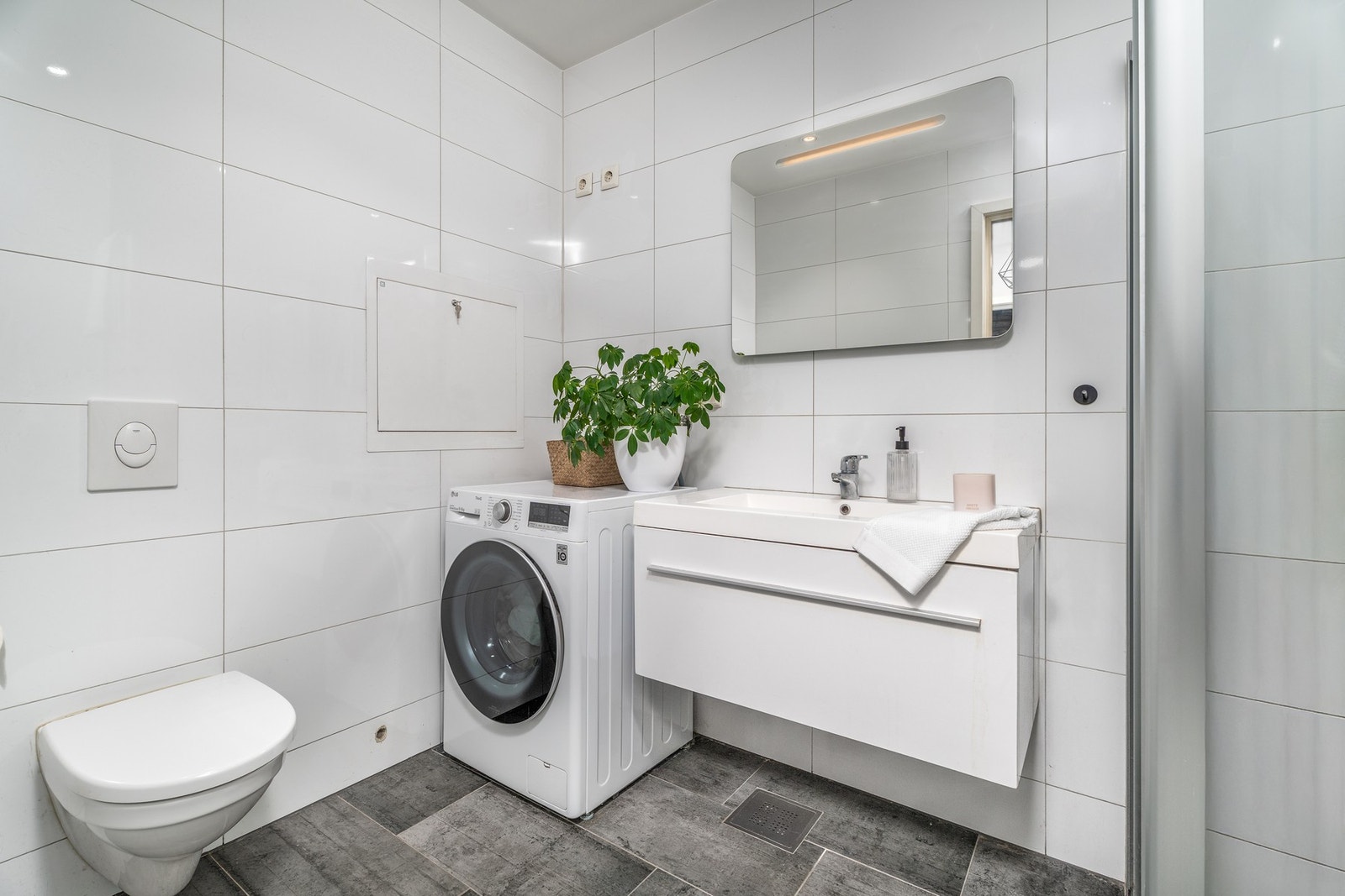 Pent og lyst flislagt bad med vegghengt innredning og wc. Det er varmekabler i gulv. Opplegg for vaskemaskin. Rør-i-rør system Galleribilde