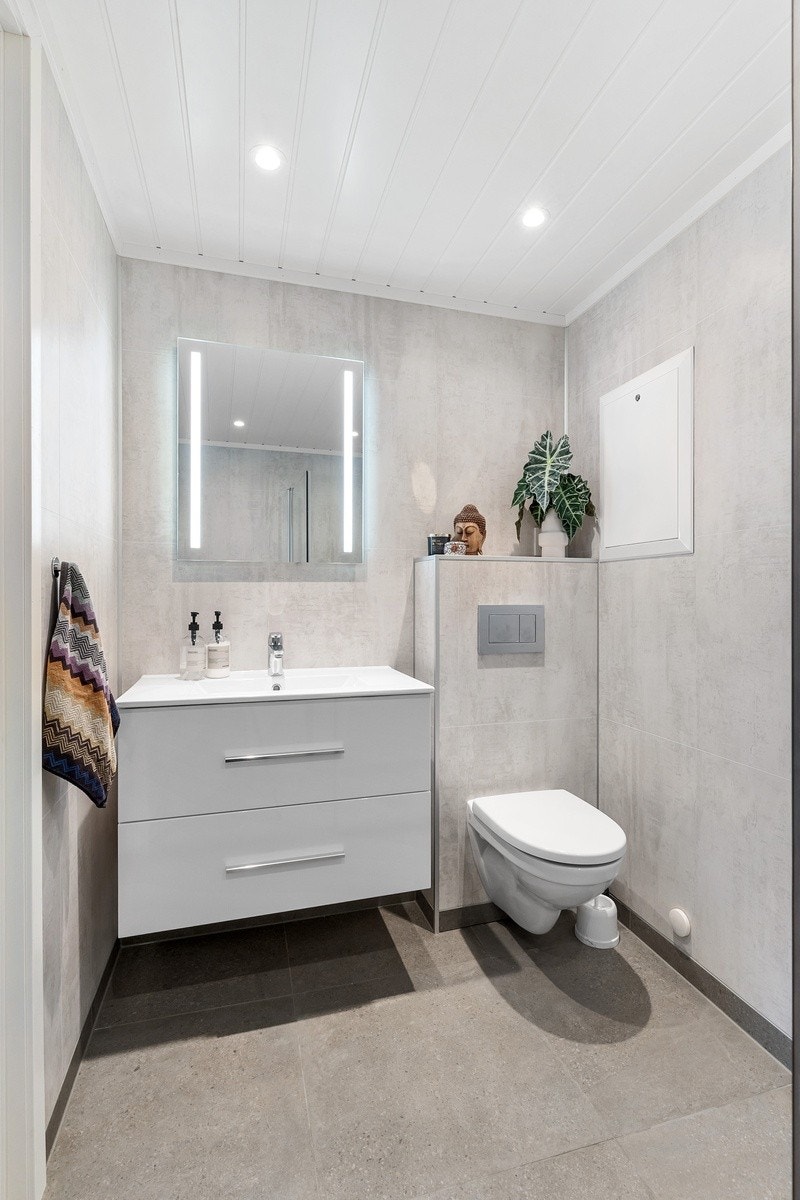 Badet i 1.etasje inneholder vegghengt toalett, dusjnisje, servant med skuffer og vegghengt speil med lys. Galleribilde